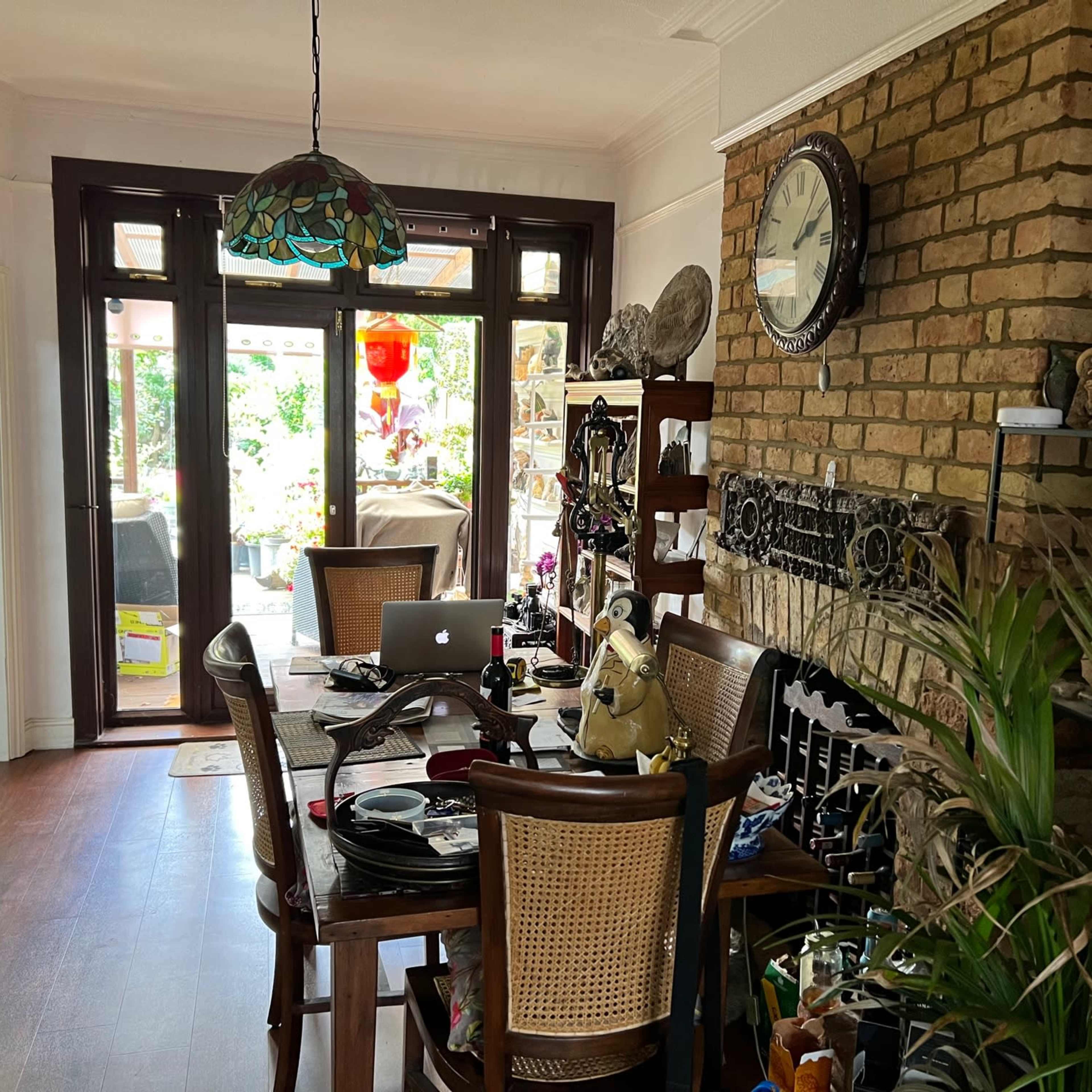 A dining area with a wooden table set for meals, a decorative brick wall, and large windows leading to an outdoor space.