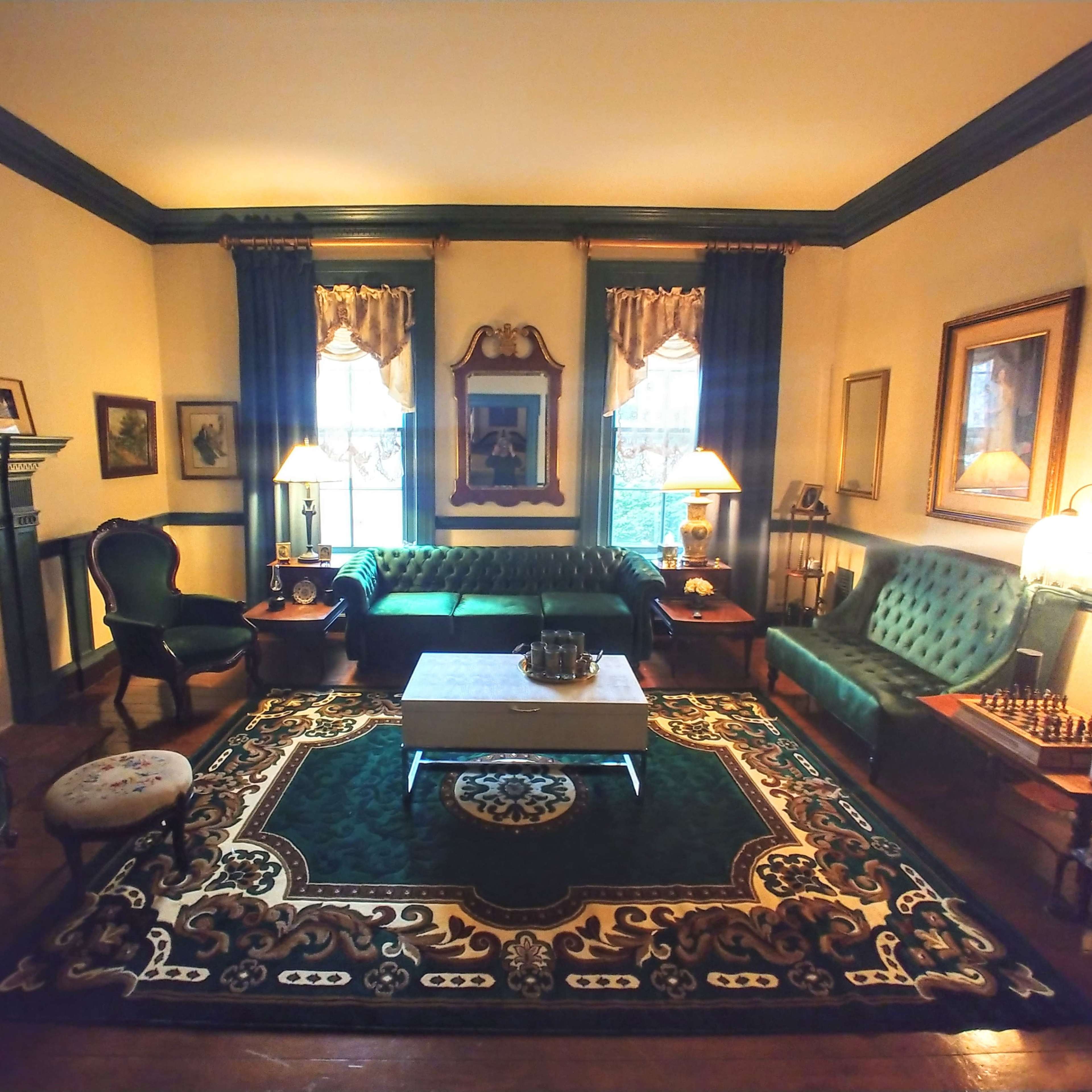 The room features green upholstered furniture, a decorative rug, a fireplace, and framed artworks on the walls.