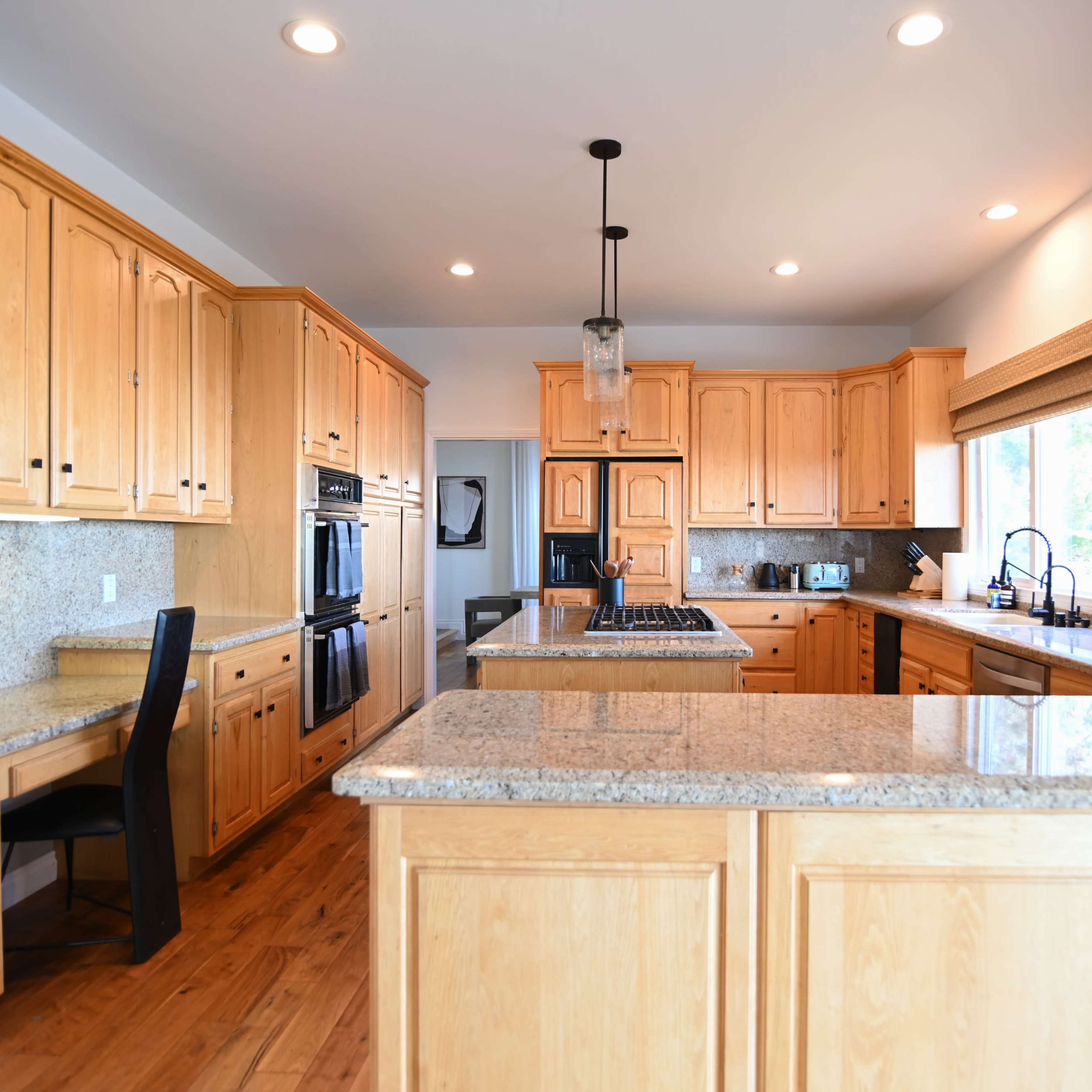 The kitchen features wooden cabinets, granite countertops, and appliances arranged around a central island with seating.