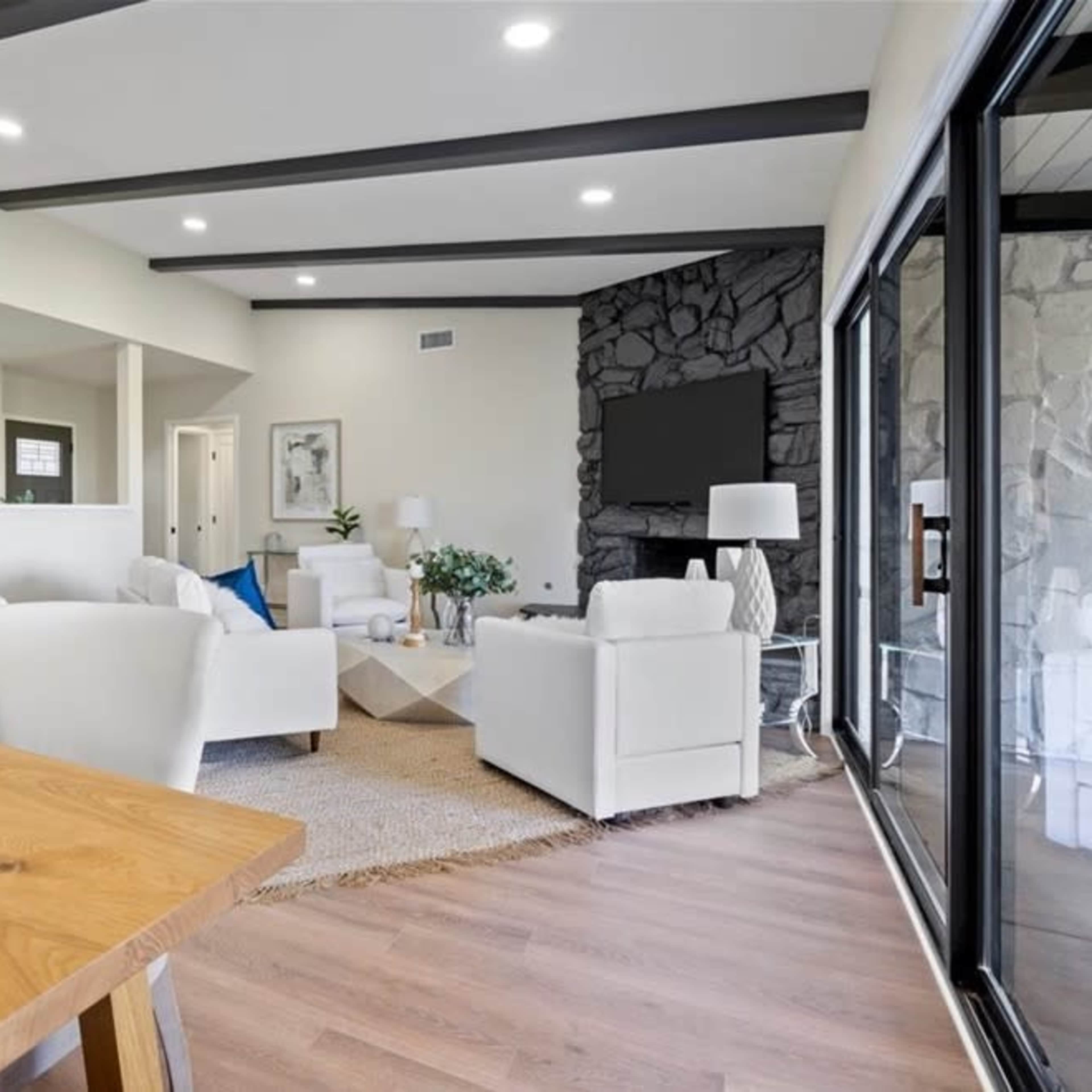 A modern living room with white furniture, a stone accent wall, and large windows that provide natural light.