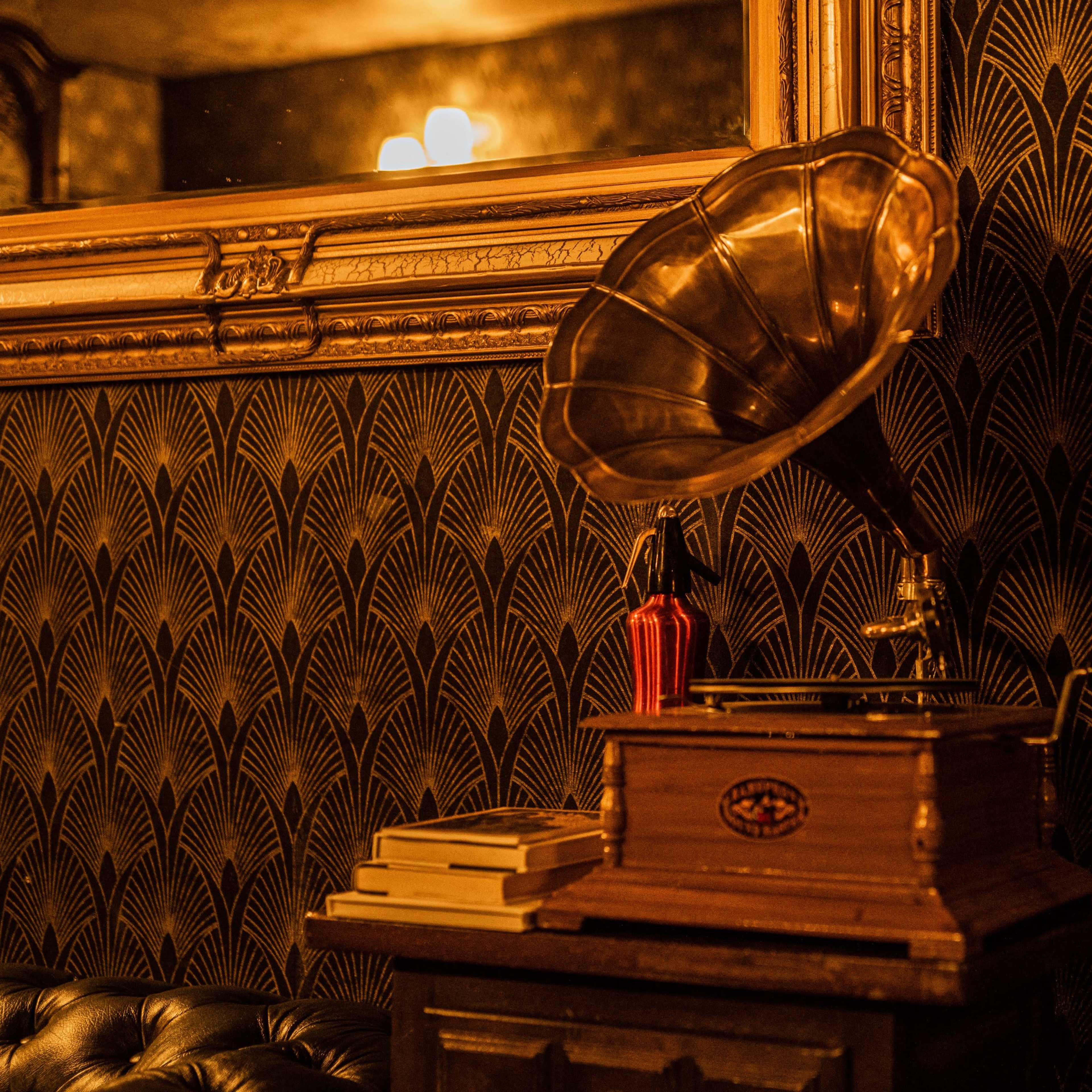 A vintage gramophone placed on a wooden table against a decorative wall with a patterned design.