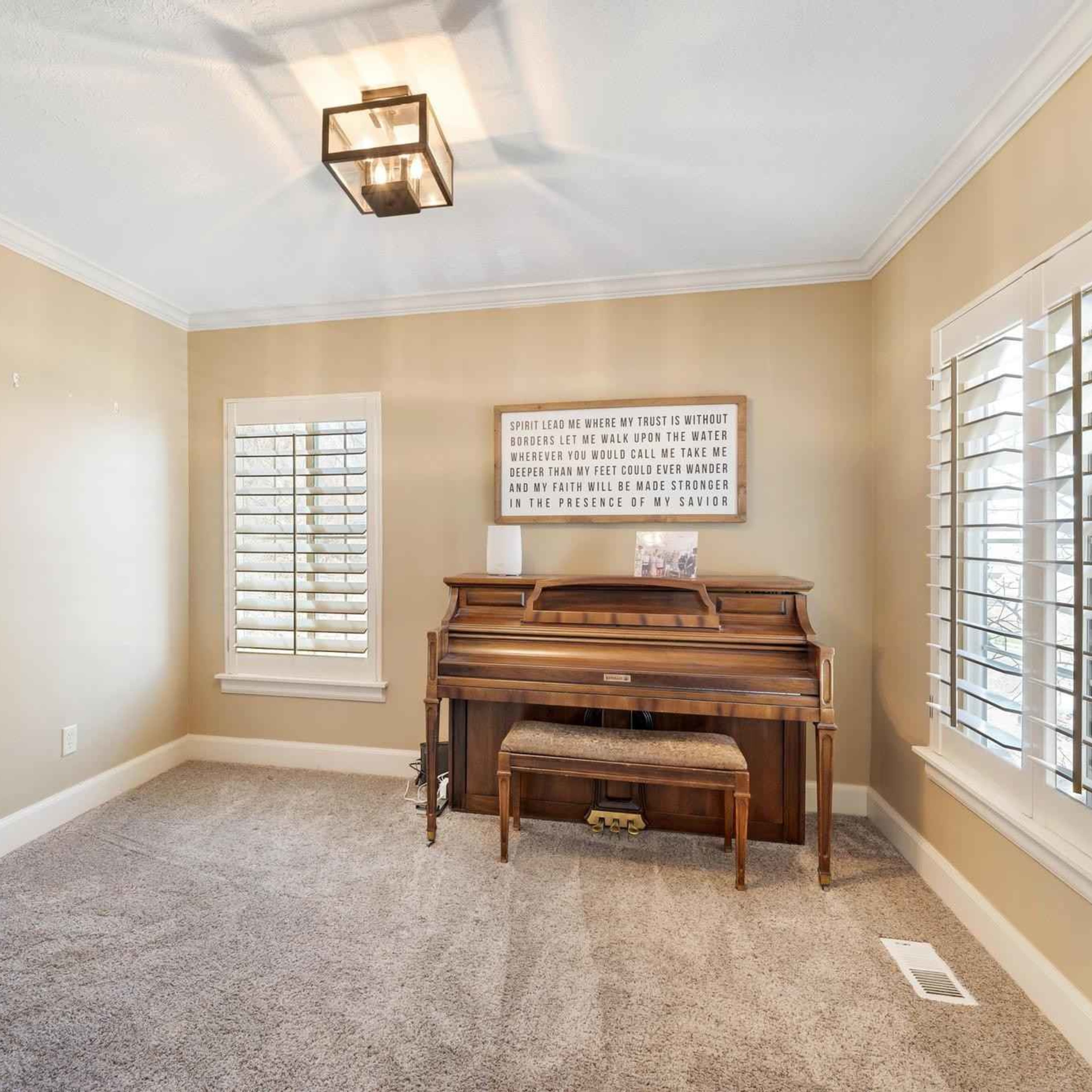 A cozy room featuring a piano against a wall, a patterned couch in the corner, and windows with plantation shutters.