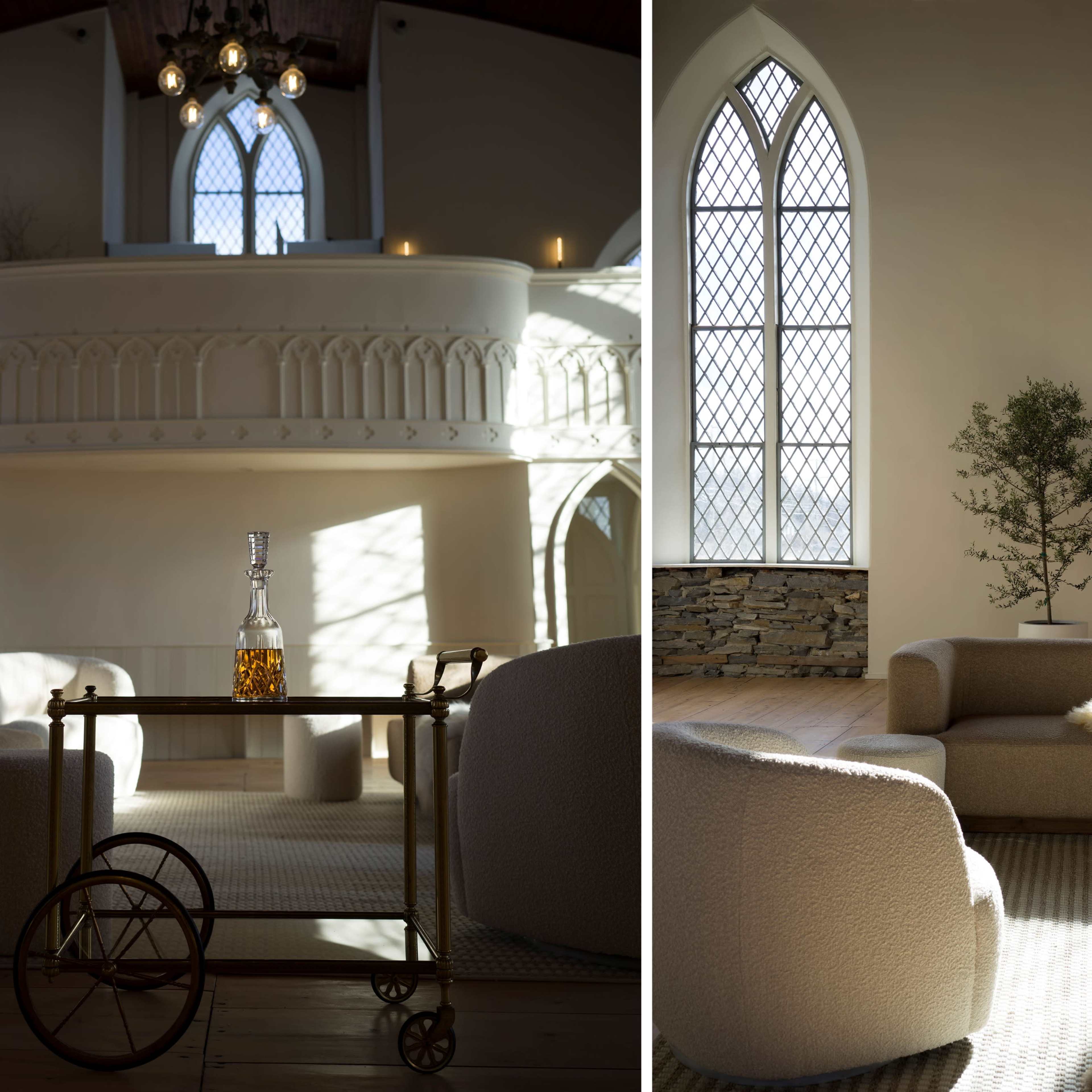 A spacious room with high ceilings, large arched windows, and modern furniture, including a circular coffee table with a bottle and a small tree in the corner.