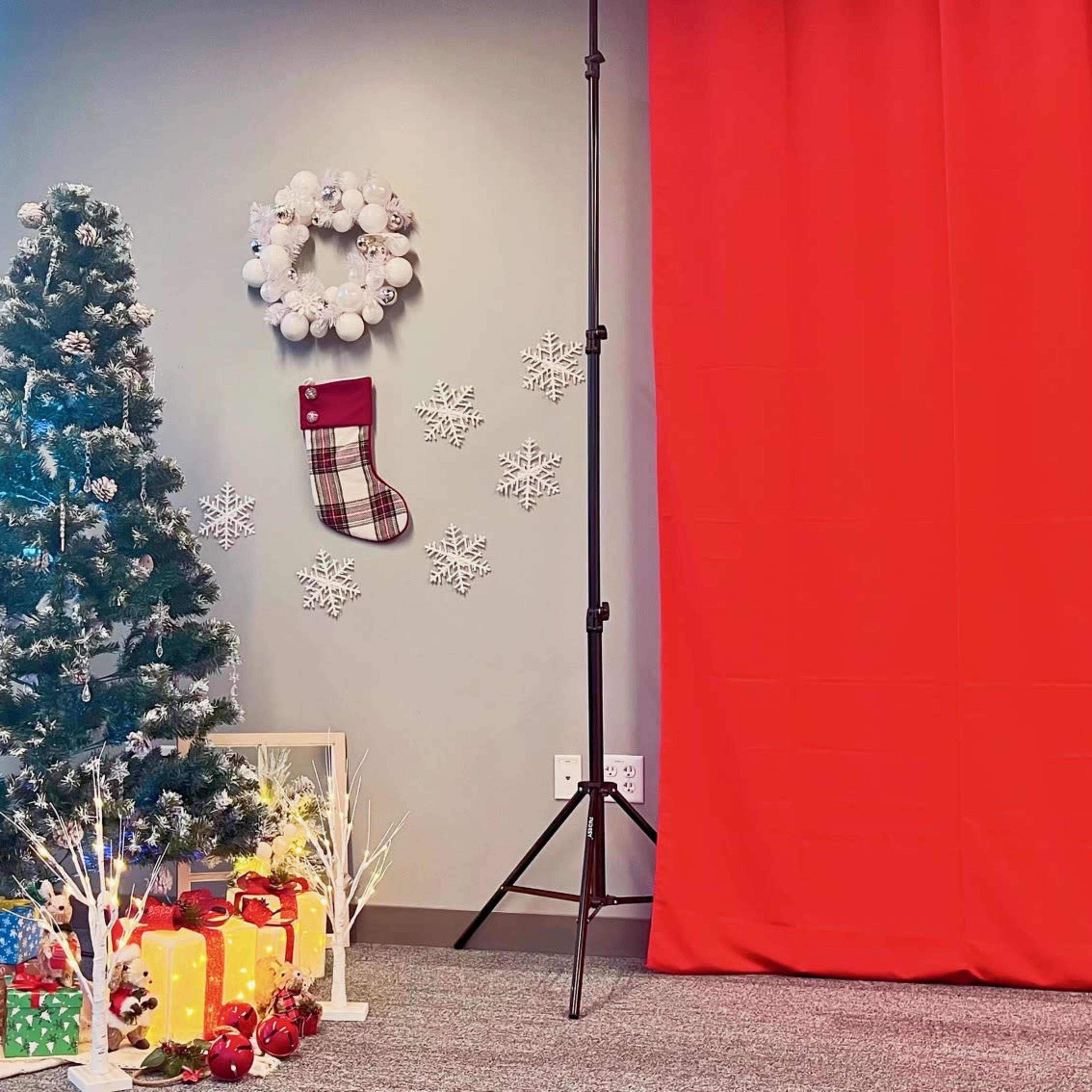A Christmas-themed display featuring a decorated tree, a stocking, and wrapped gifts arranged beside a red curtain in an indoor space.