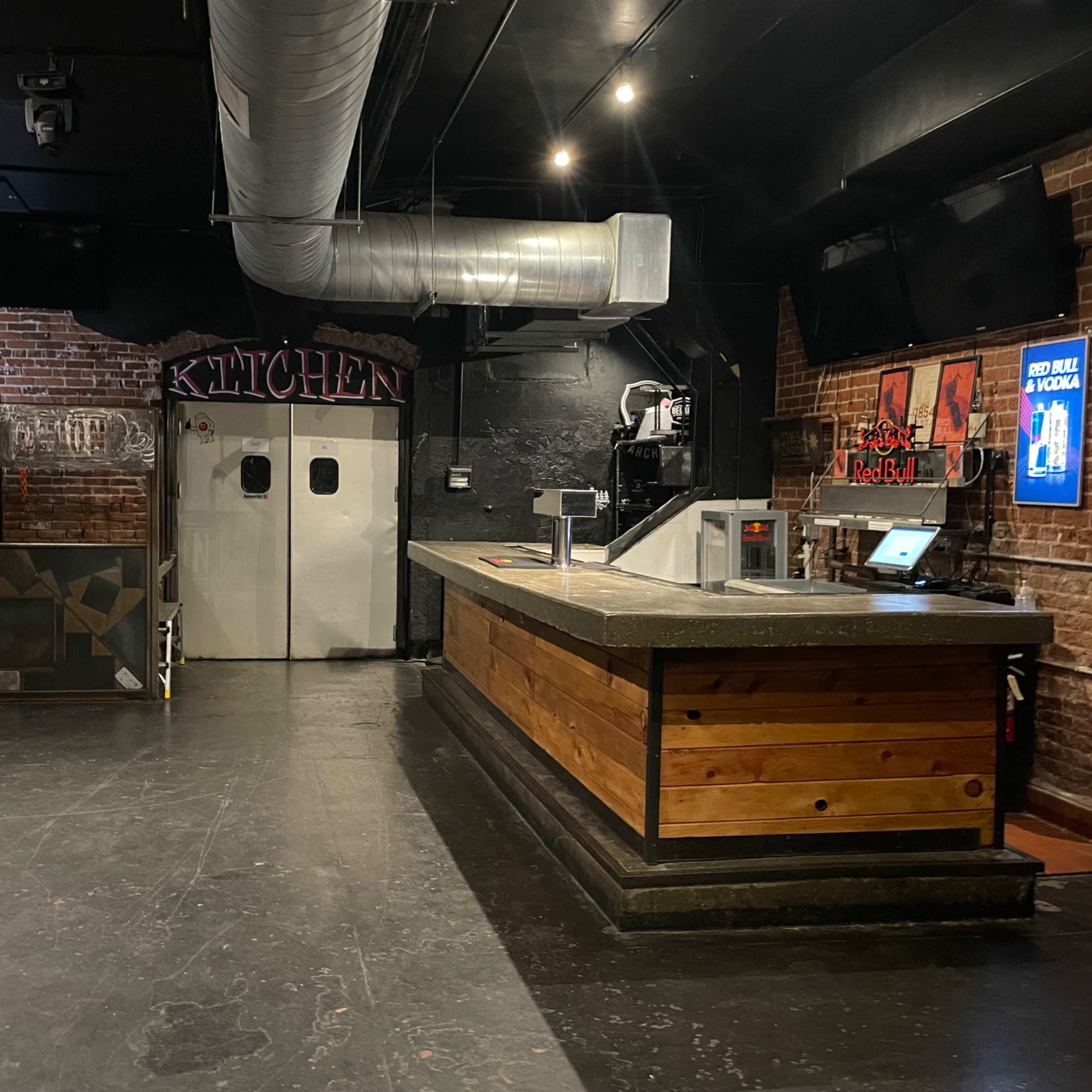 An industrial-style kitchen area with a wooden counter and large metal doors in a dimly lit space.