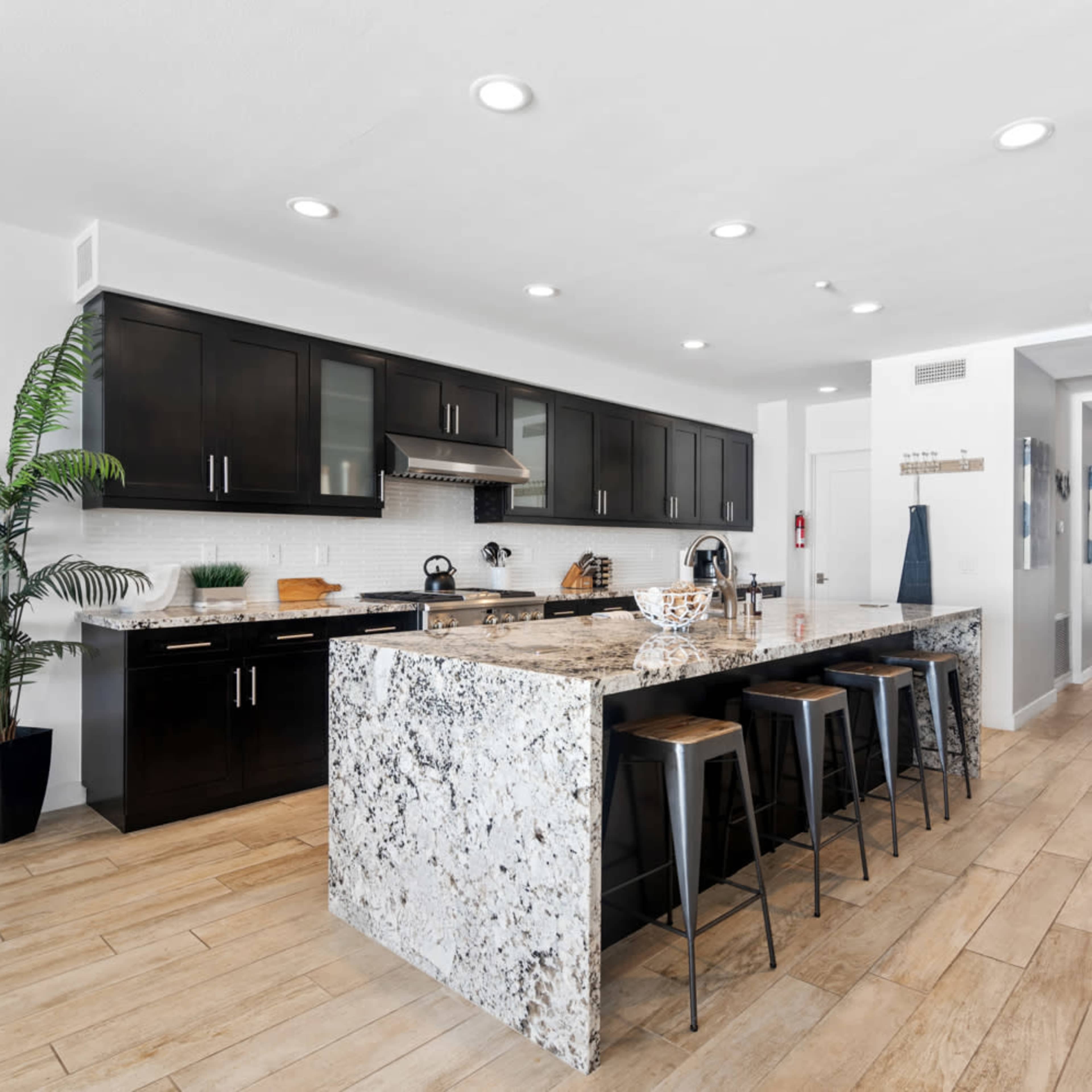 A modern kitchen with black cabinetry, a granite island with seating, and light wood flooring.