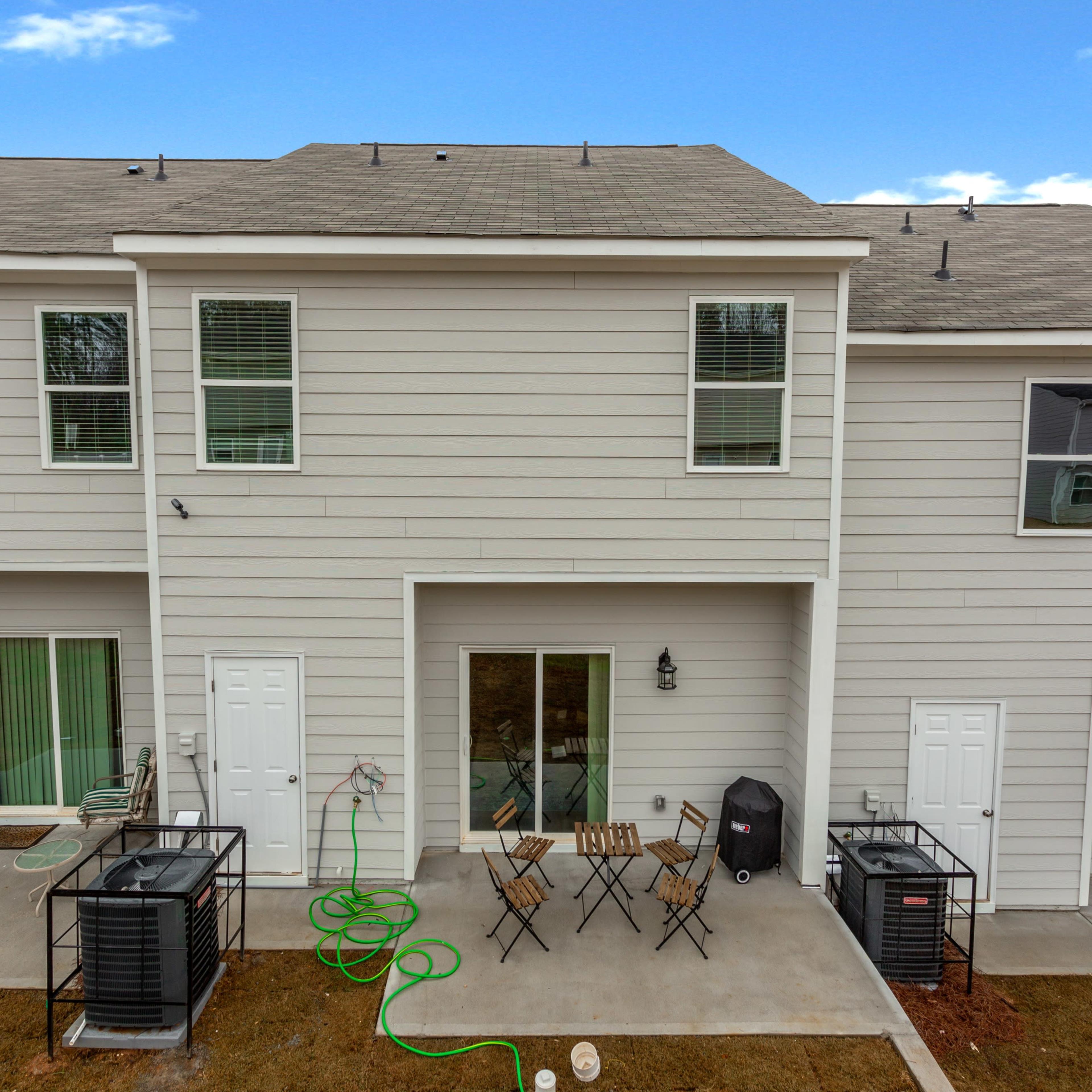 The back view of two adjacent townhouses with patios, chairs, and air conditioning units.