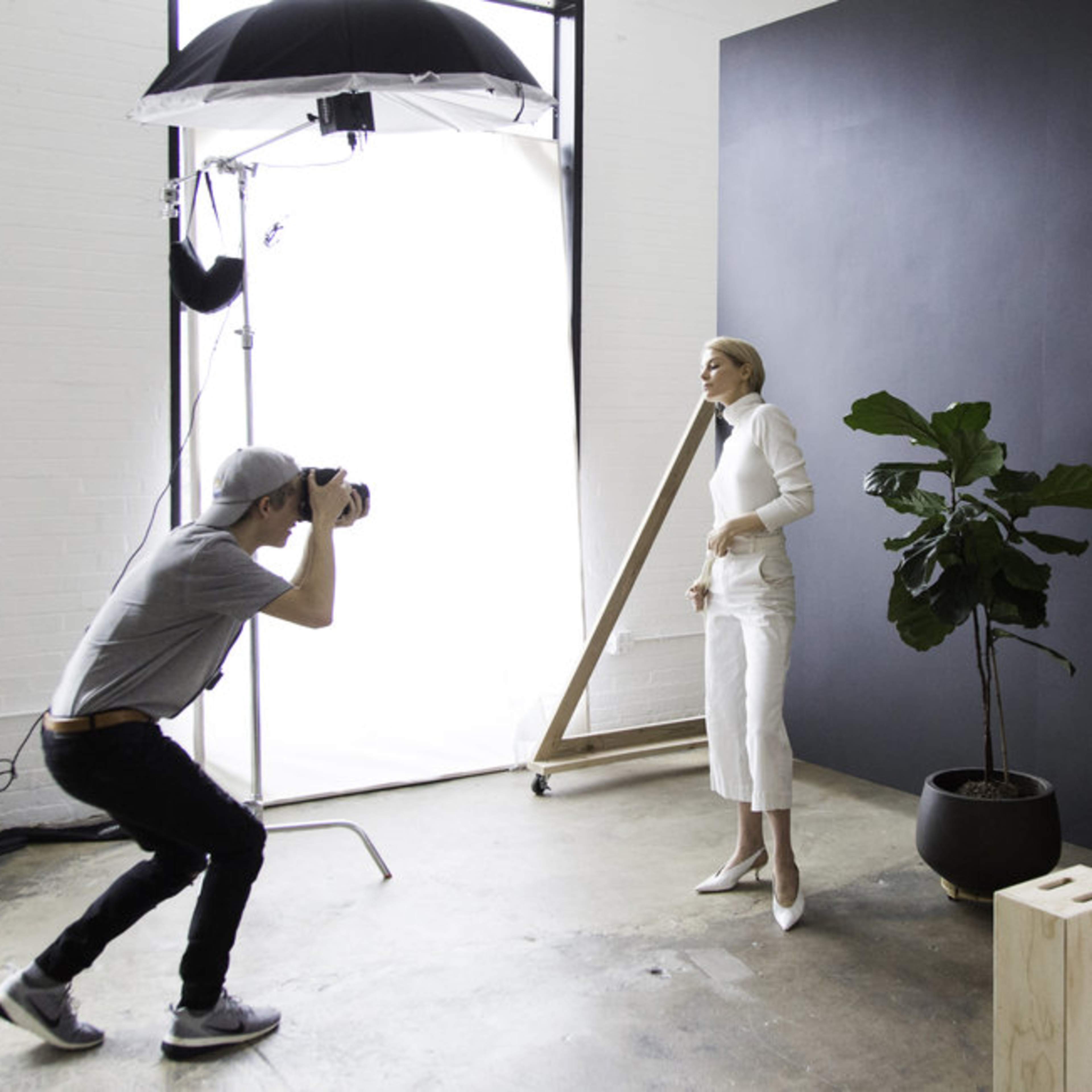 A photographer captures an image of a model posing in front of a black backdrop in a studio setting.