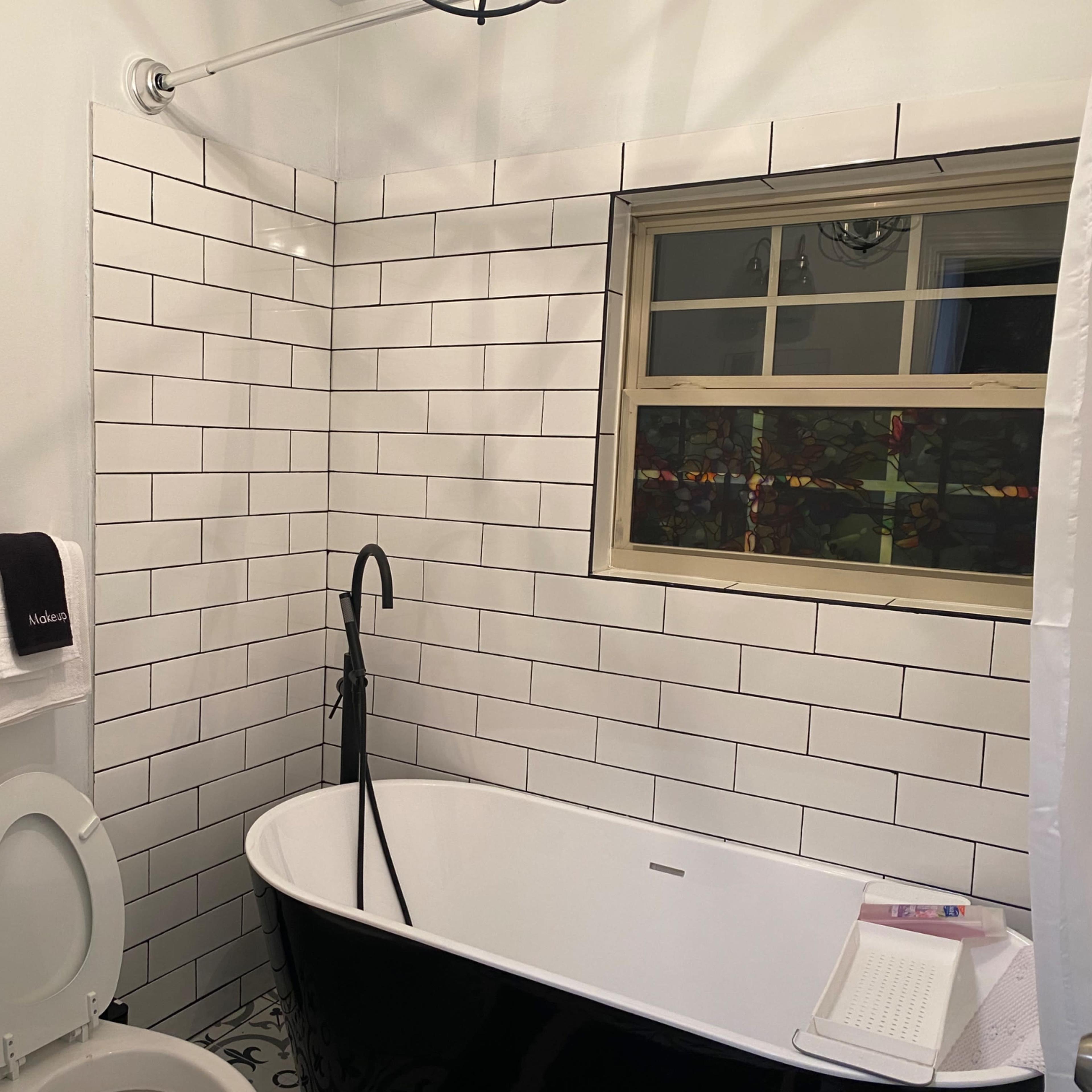 A modern bathroom featuring a black and white color scheme with a freestanding tub, a toilet, and tiled walls.