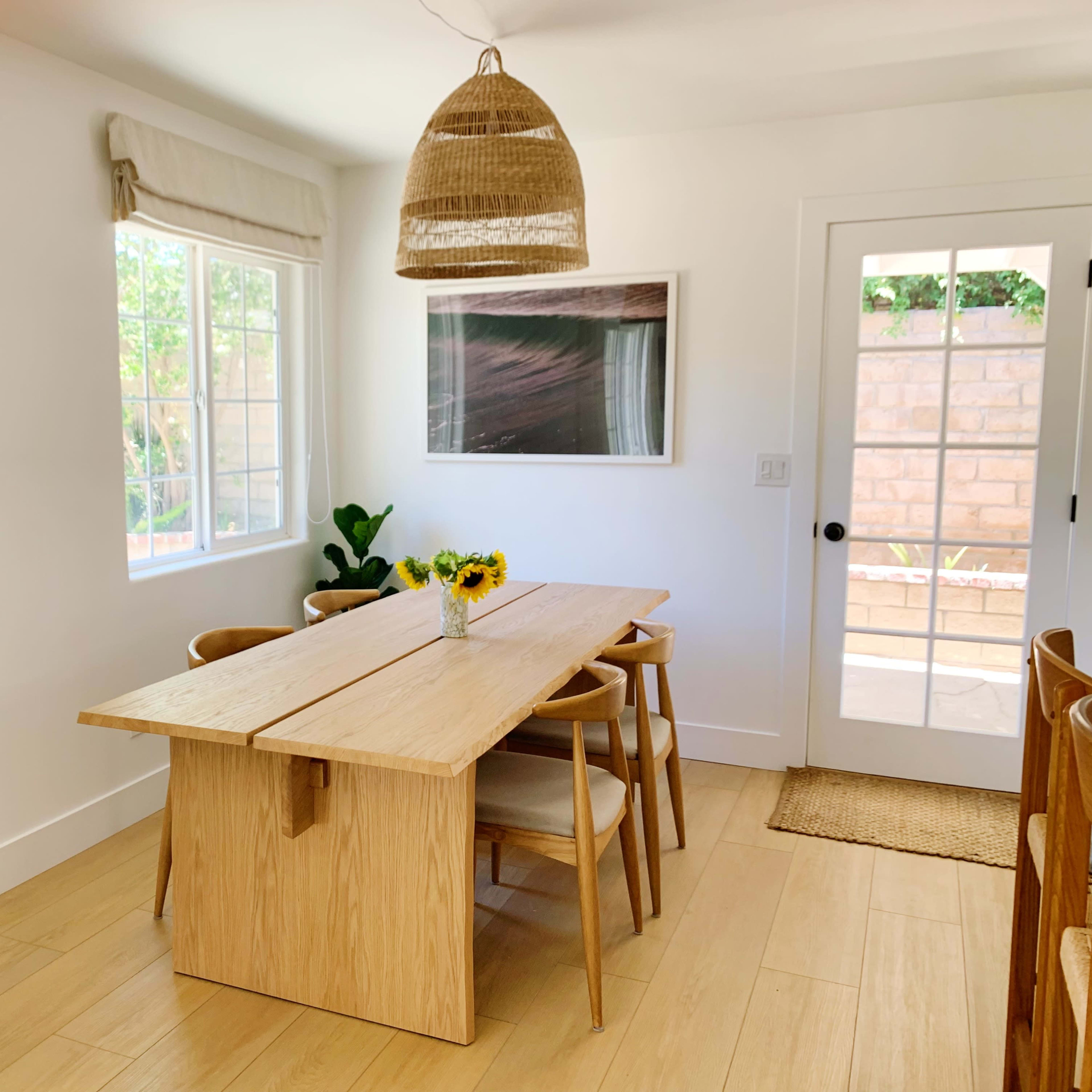 A well-lit dining area features a wooden table with sunflowers, surrounded by chairs, and a large window letting in natural light.