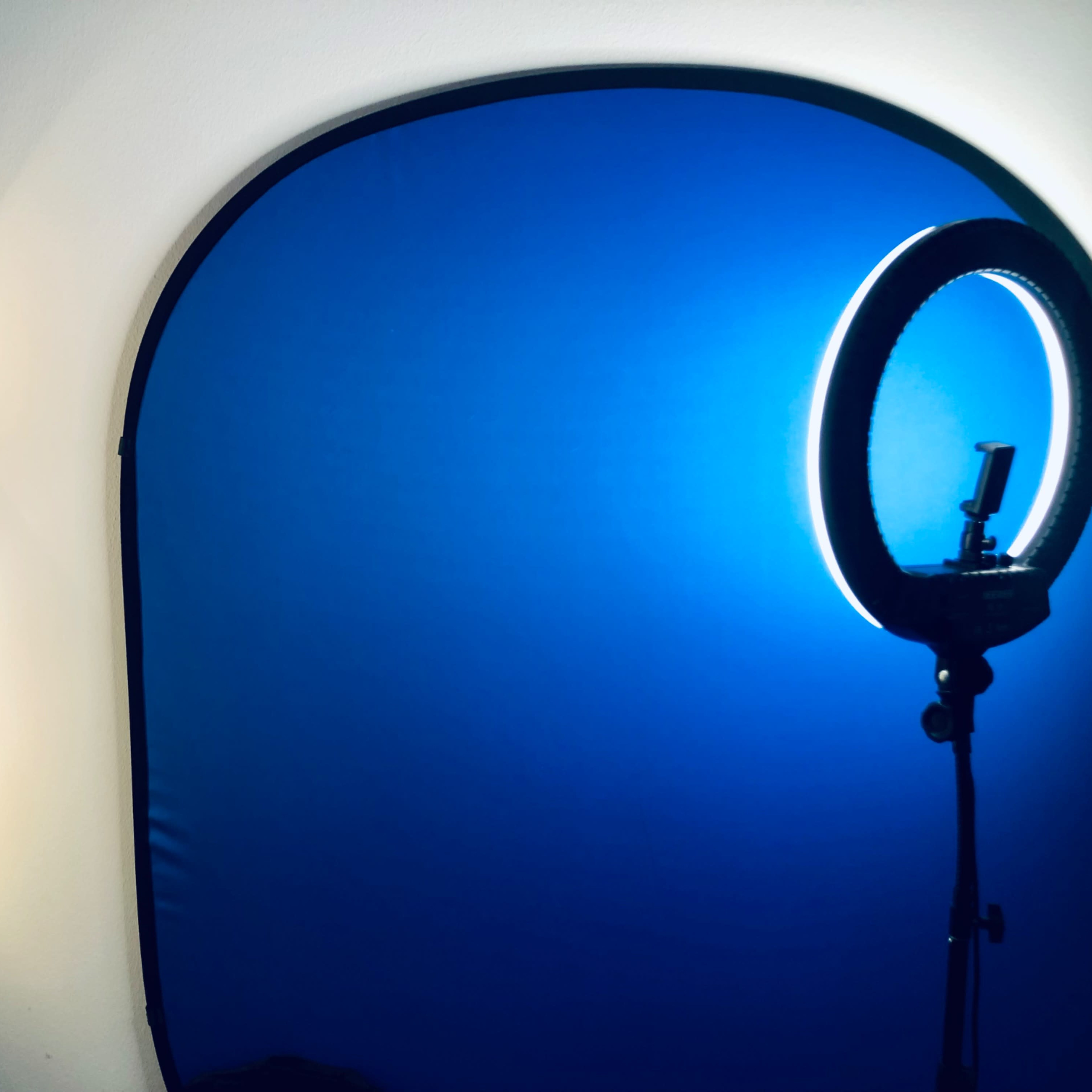 Three light fixtures mounted on a wall beside a circular light ring set against a blue backdrop.