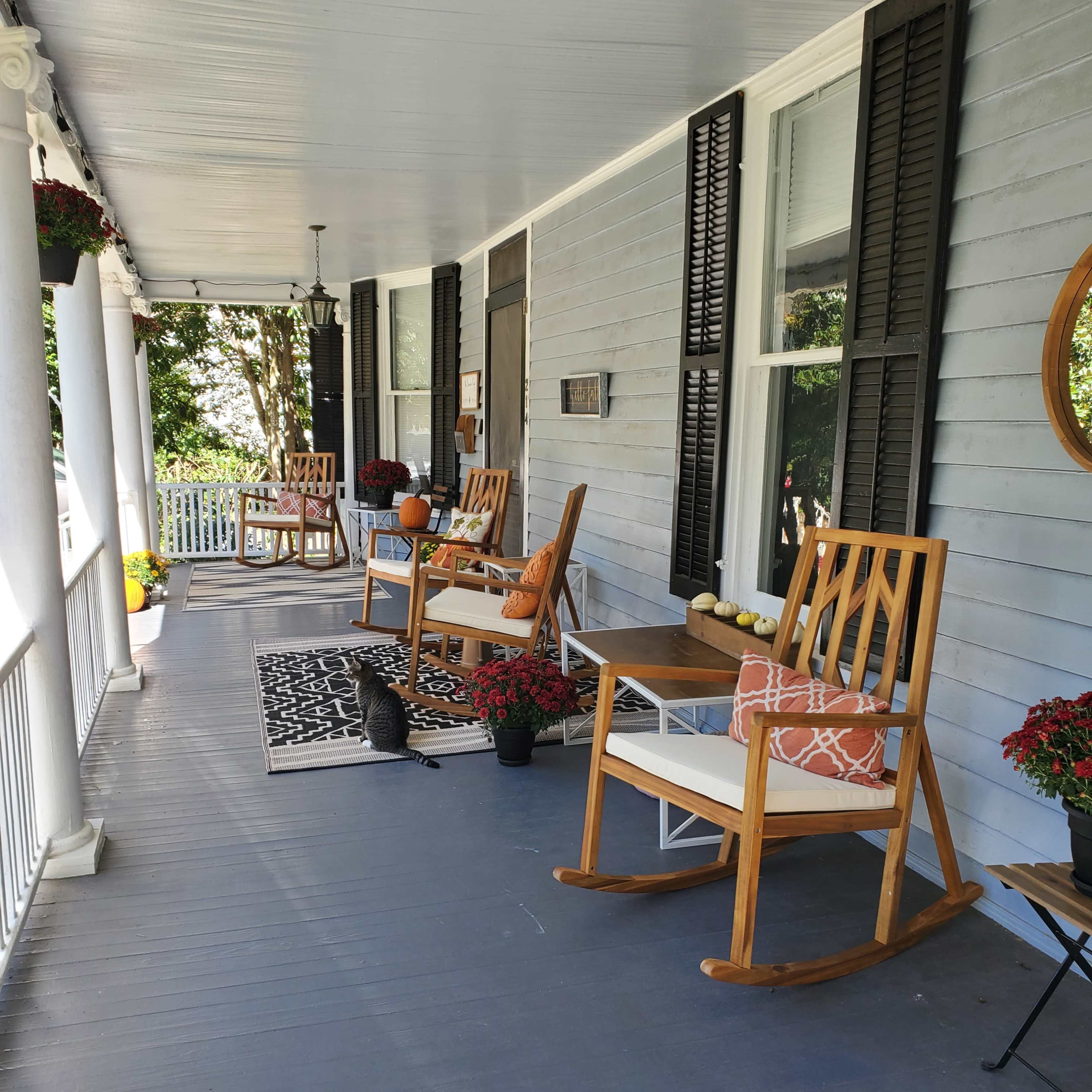 A porch with wooden rocking chairs, potted flowers, and a patterned rug.