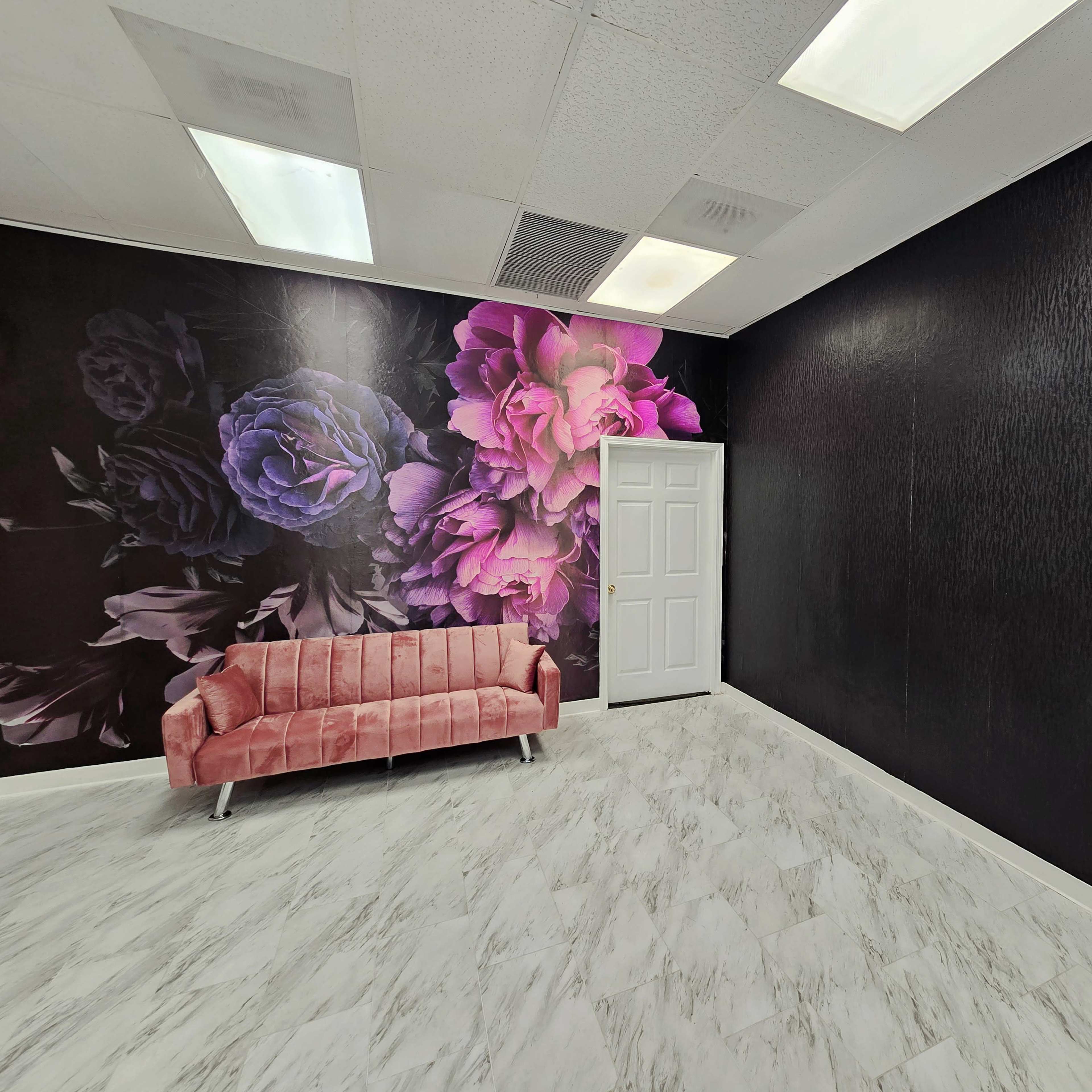 A room with a floral accent wall, a light-colored marble floor, and a pink velvet sofa against the wall.
