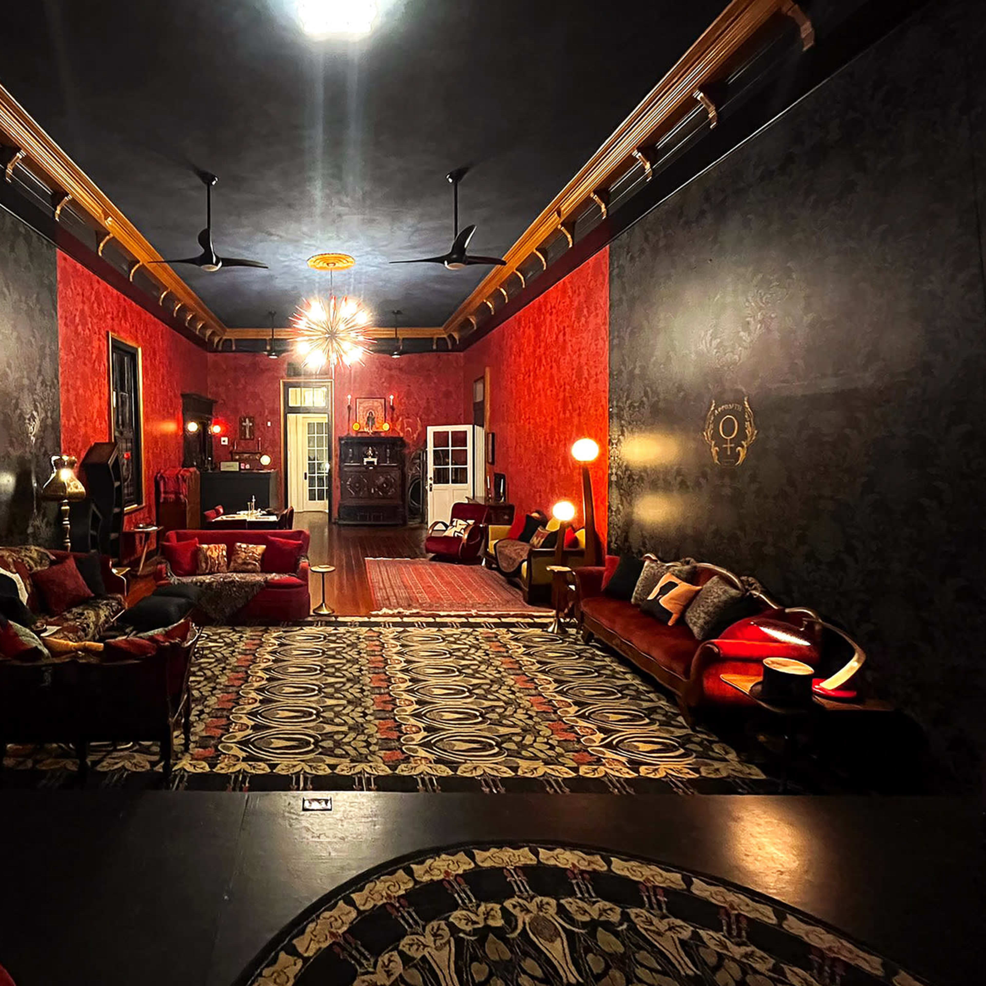 A dimly lit lounge with red and black walls, featuring ornate furniture and decorative lighting.