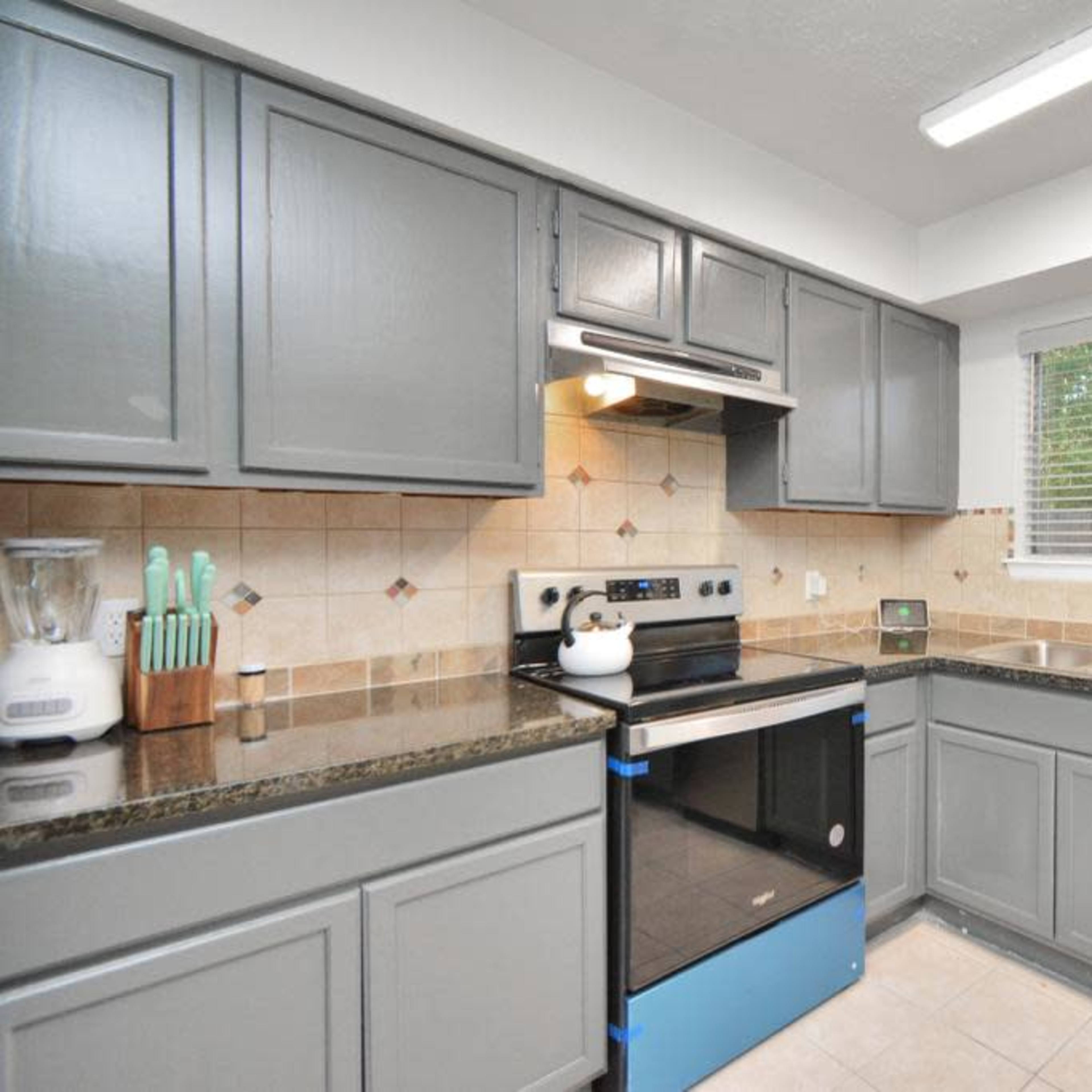 A kitchen features gray cabinets, stainless steel appliances, a tile backsplash, and a window with natural light.