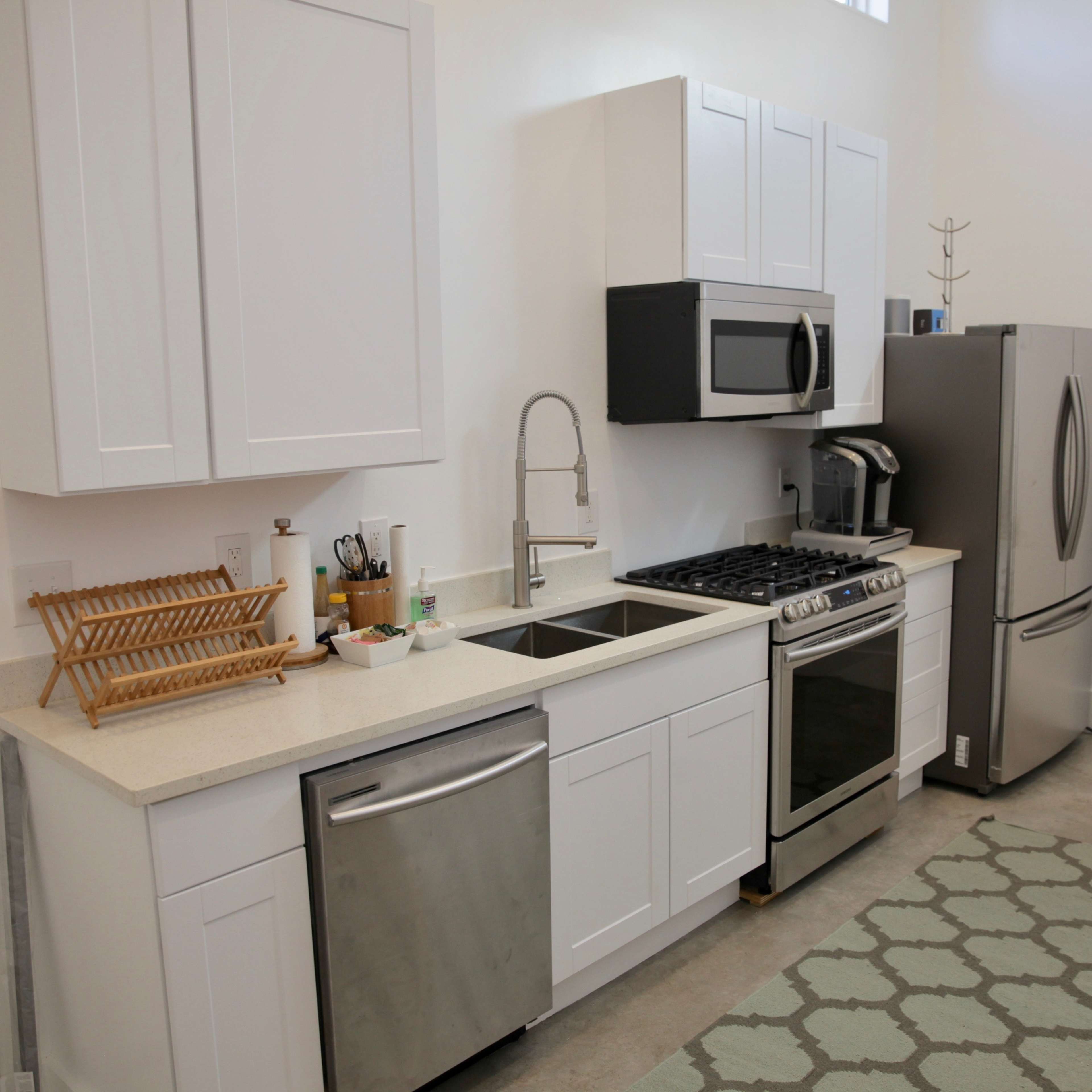A modern kitchen features white cabinetry, stainless steel appliances, a double sink, and a countertop with a dish drying rack.
