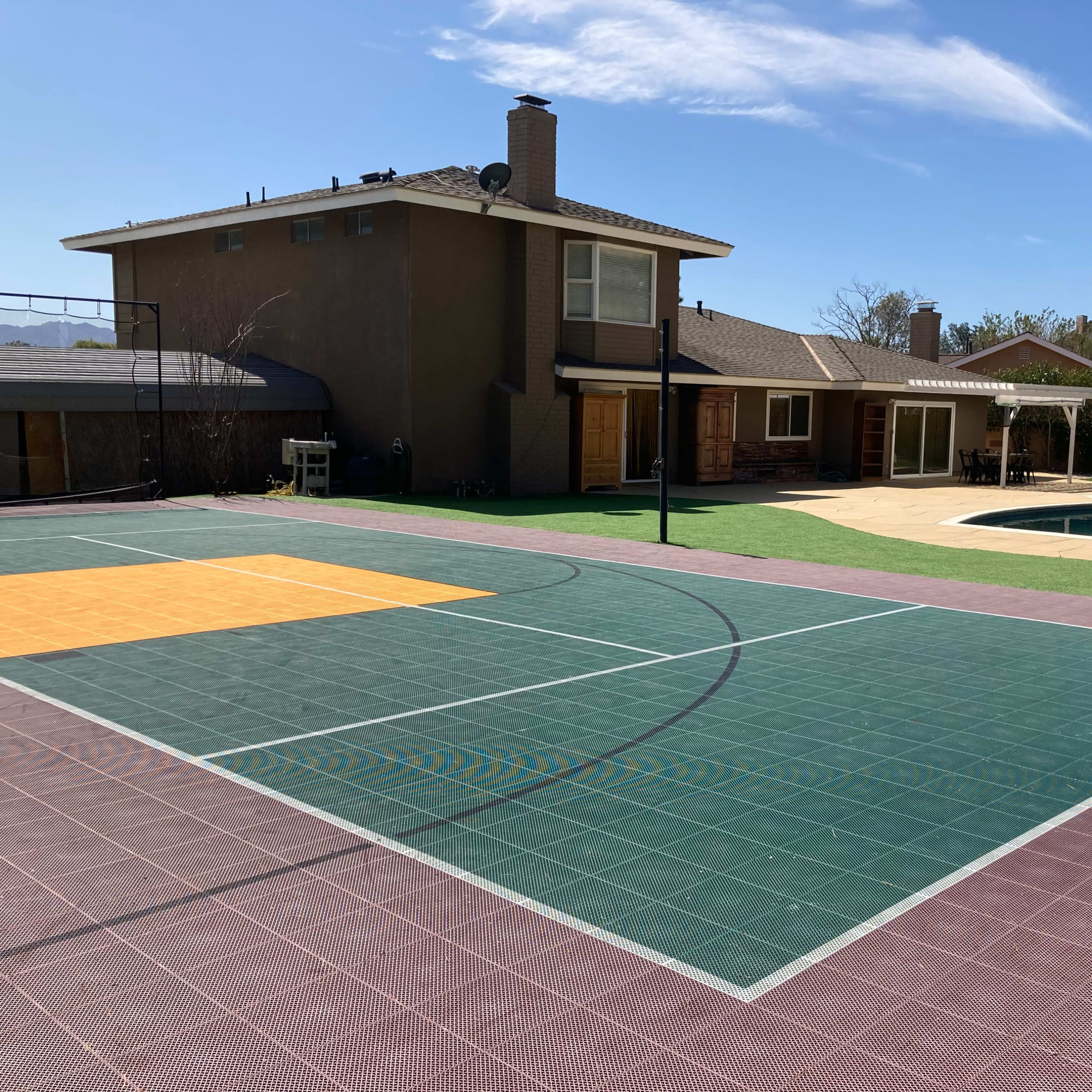 A basketball court in the foreground, with a swimming pool and a two-story house visible in the background.