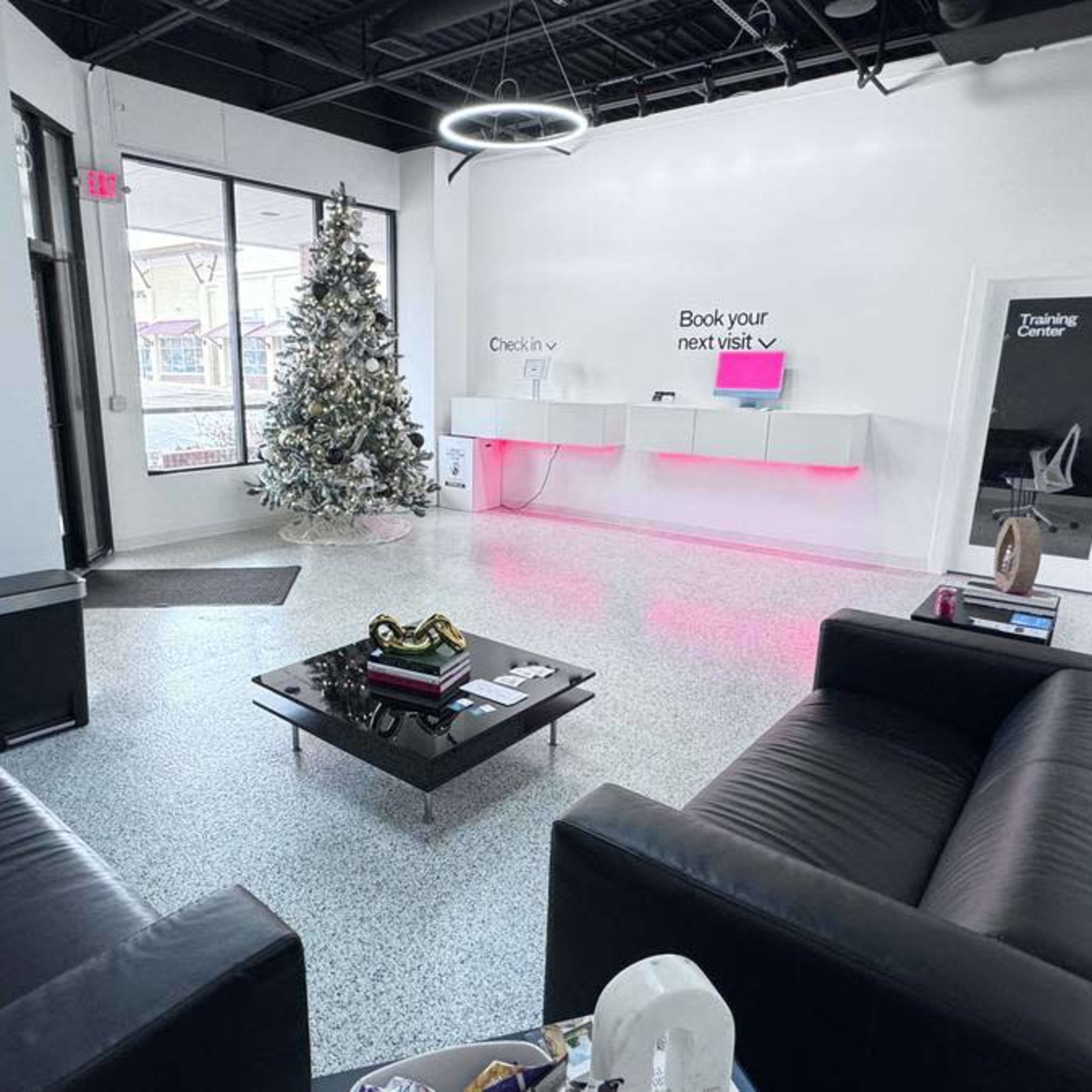 A modern reception area featuring two black leather sofas, a coffee table with various items, and a decorated Christmas tree in the corner.
