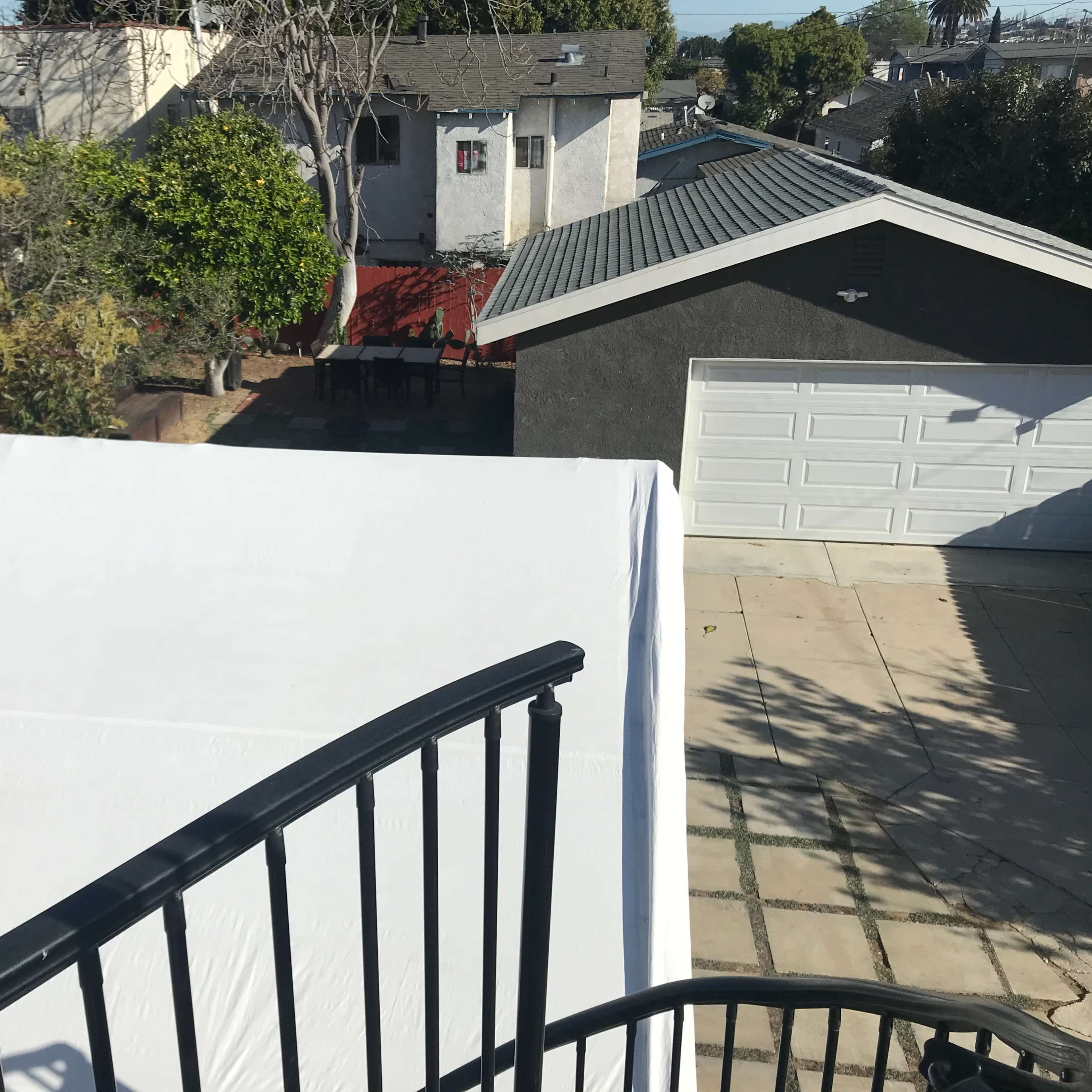 A view from an elevated position overlooking a backyard with several trees, a red structure, and a gray garage.