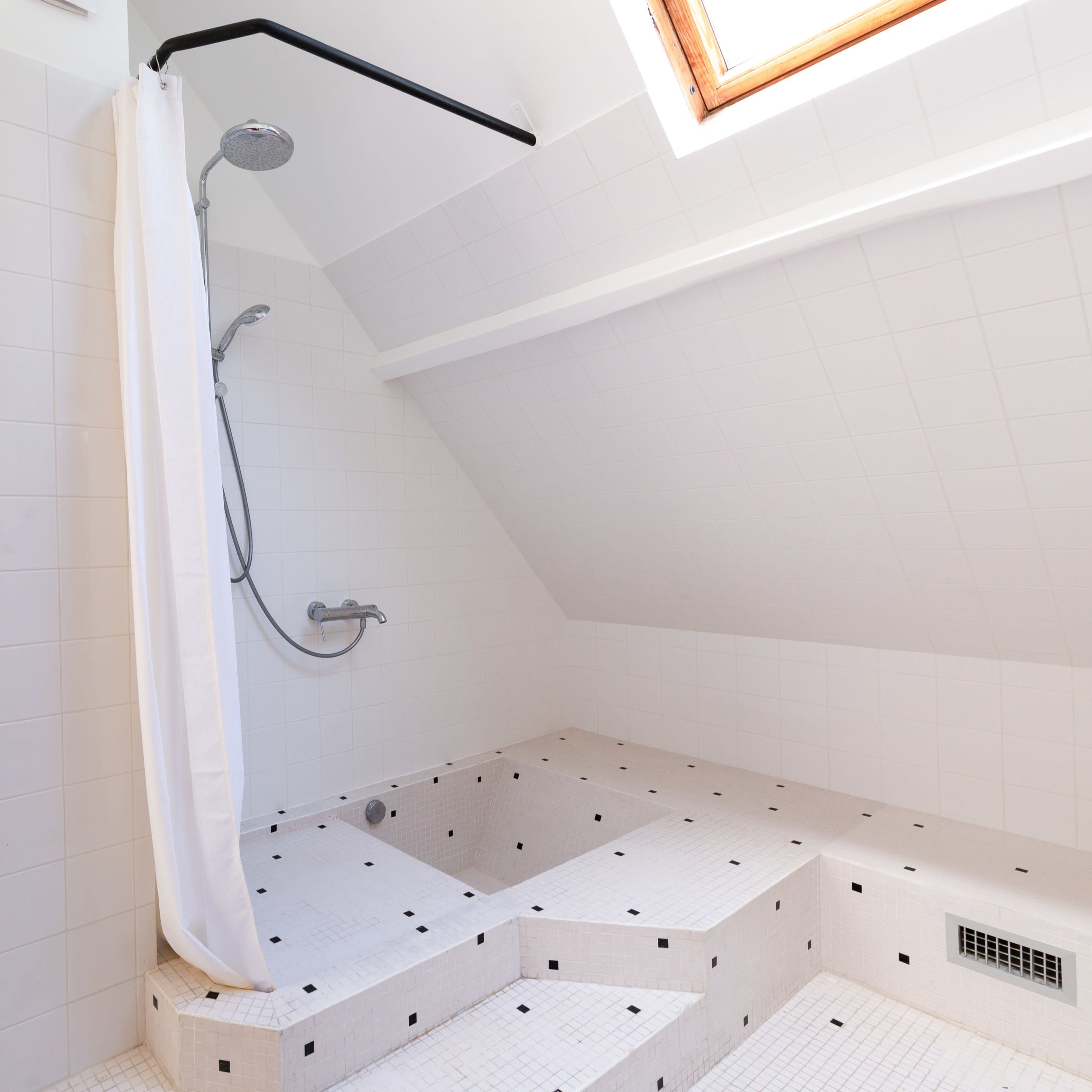 A modern bathroom featuring a walk-in shower with a curved wall, a glass block window, and a sunlit ceiling.