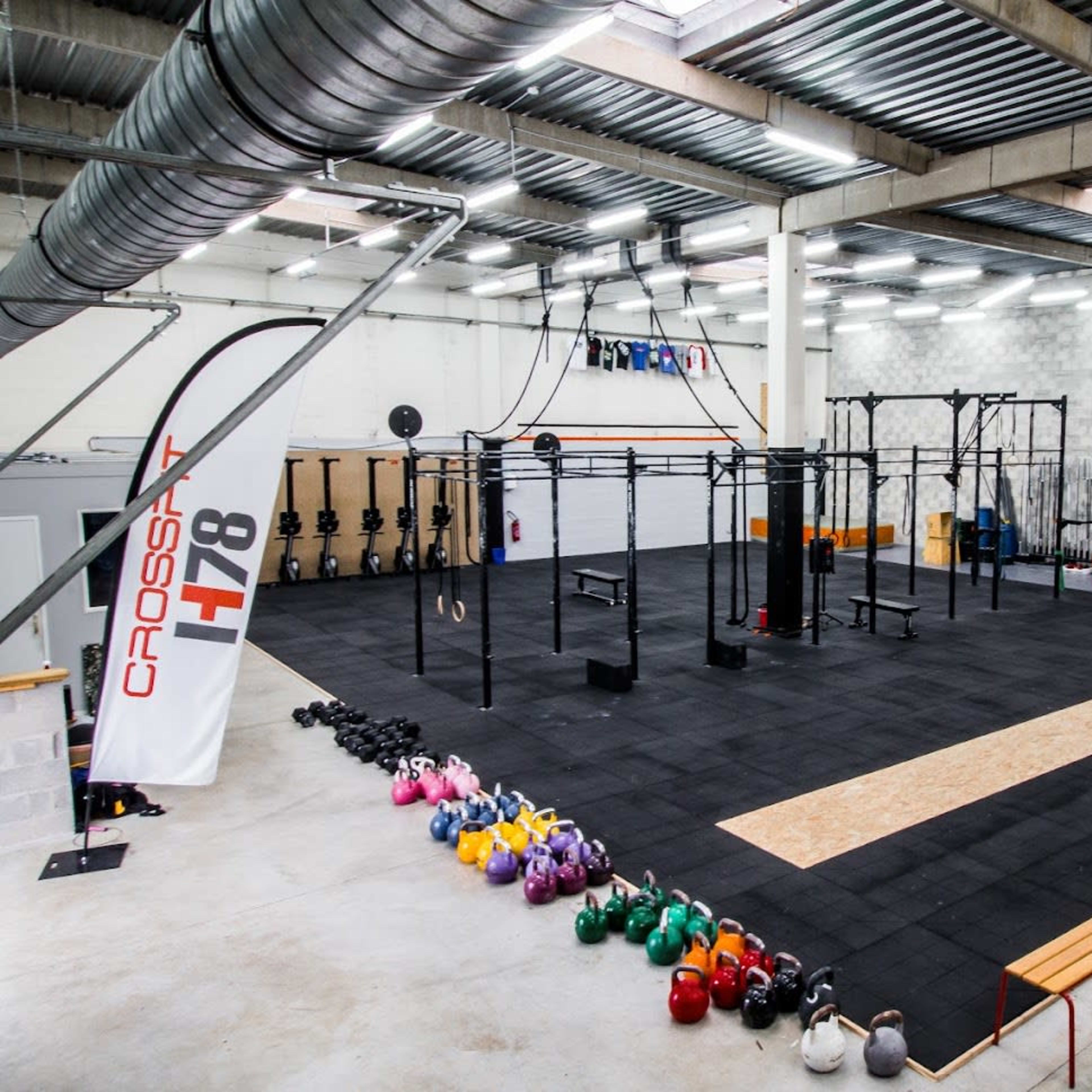 A spacious gym area equipped with various workout stations, kettlebells arranged along one side, and a large open floor for exercises.