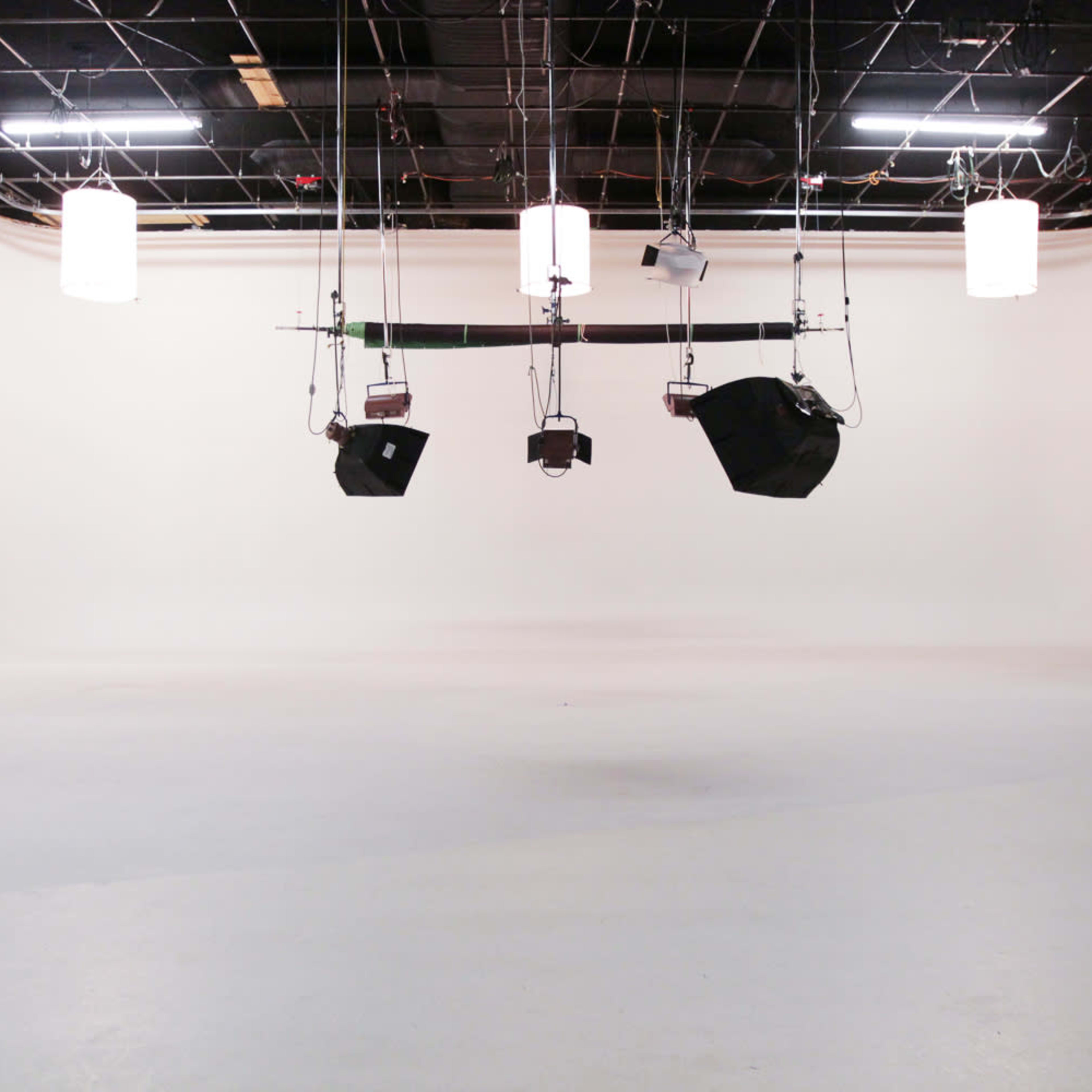 A blank photography studio with a white backdrop and suspended lighting equipment.