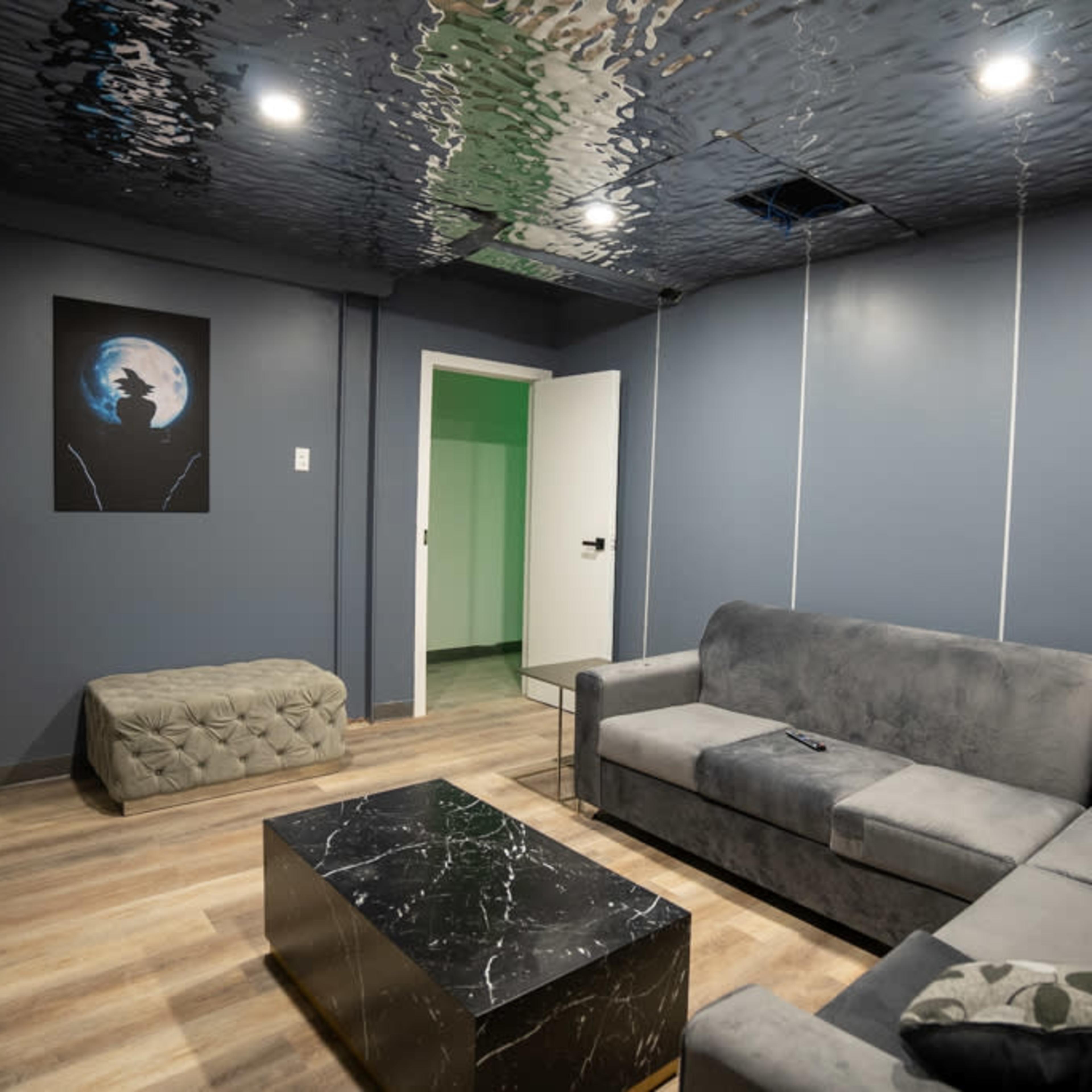 A modern living room featuring a gray sectional sofa, a black marble coffee table, and a ceiling that reflects light with a wavy appearance.
