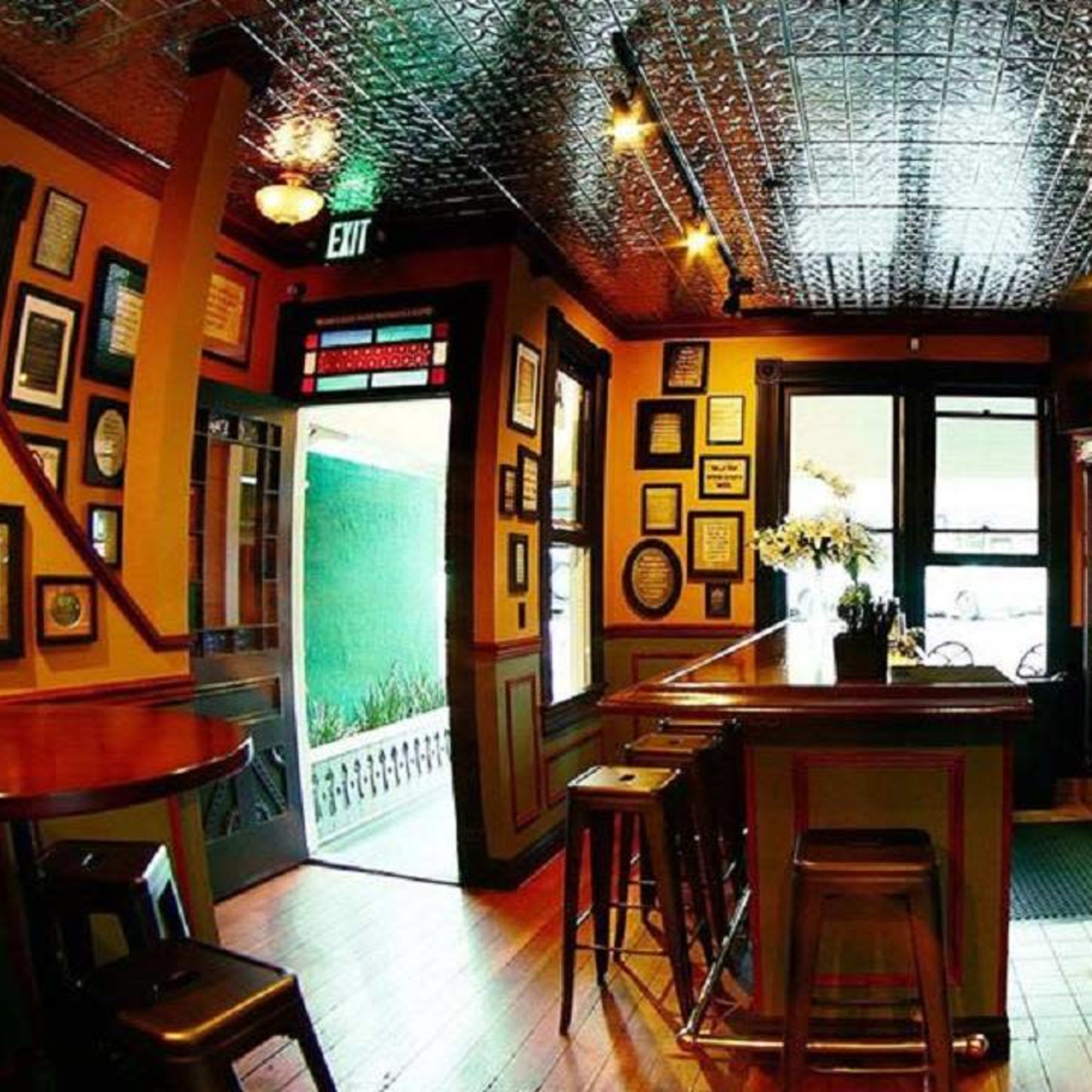 A cozy bar with wooden floors, a long counter, and walls adorned with framed pictures and decorations.