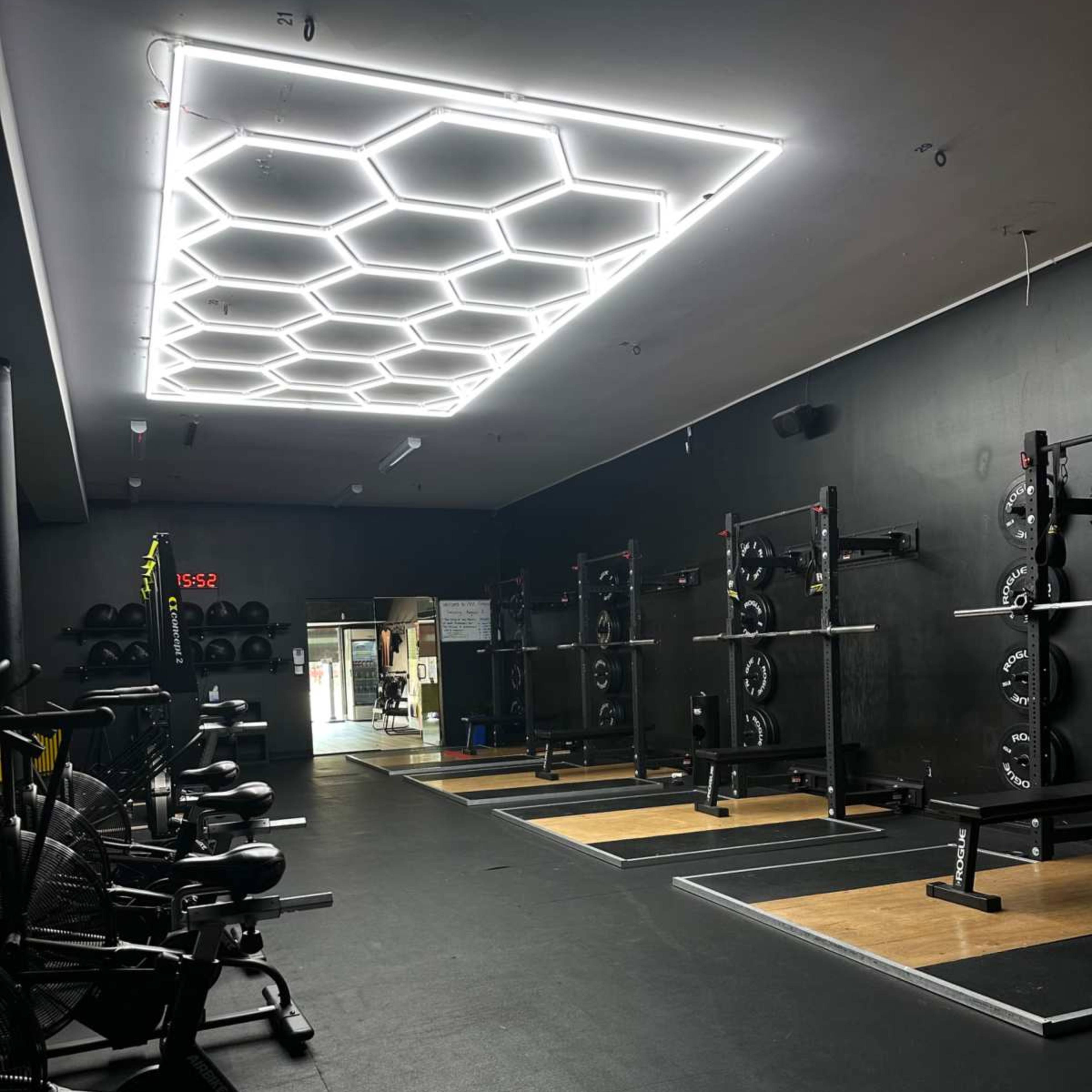 A gym interior featuring weightlifting equipment arranged on a floor with a hexagonal light fixture overhead.