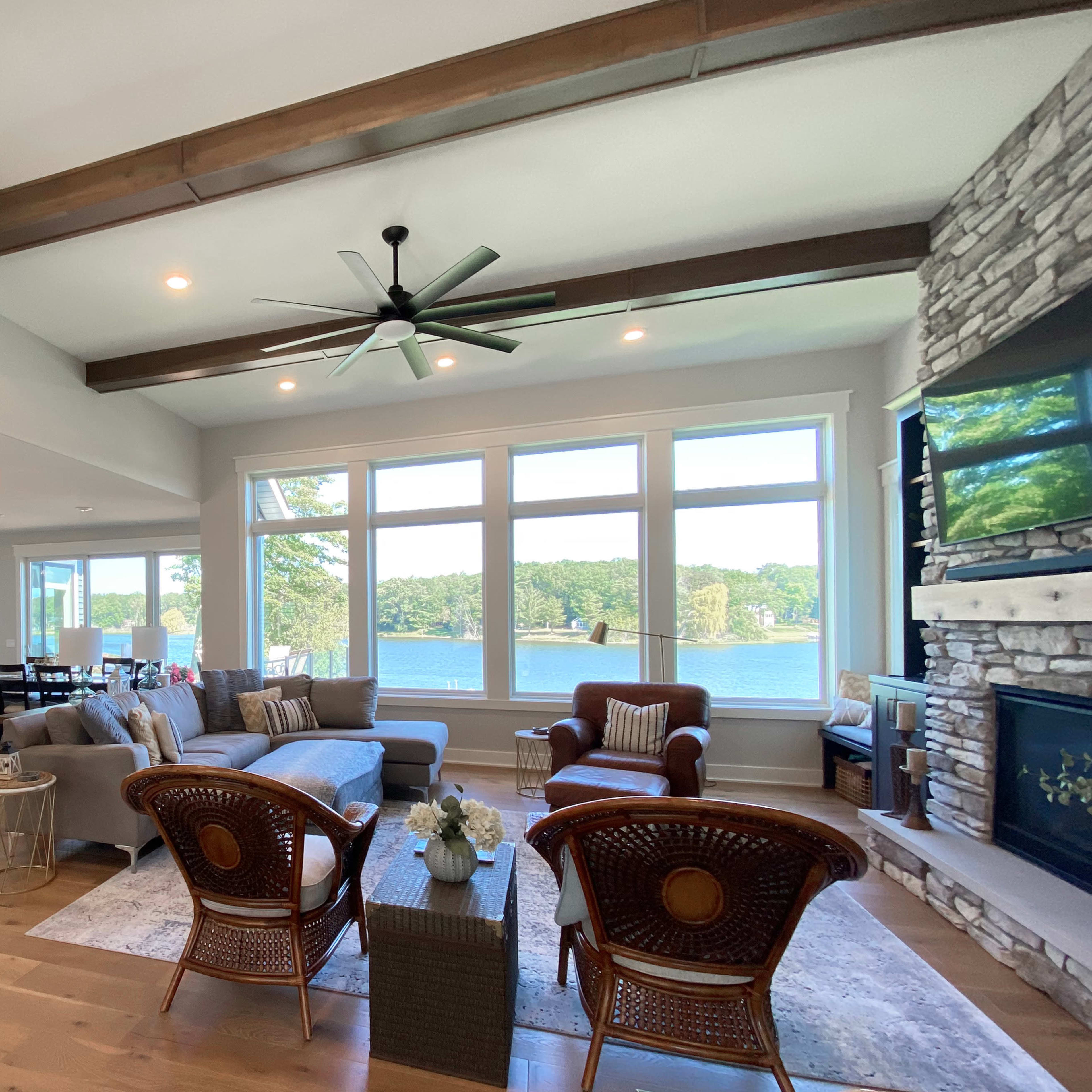 A spacious living area features a comfortable seating arrangement with large windows showcasing a view of a lake.