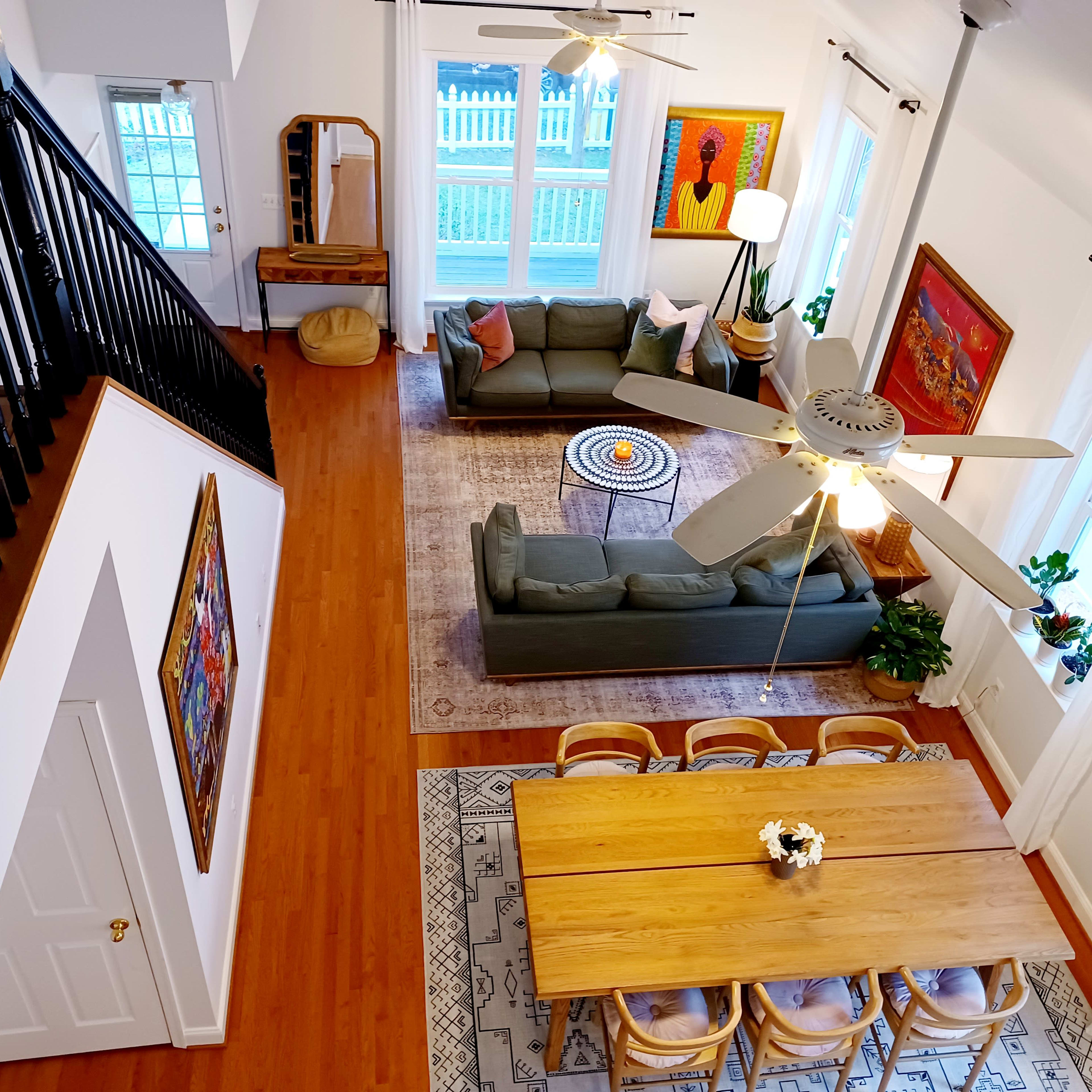 A well-lit, two-story living space with a green sofa, wooden dining table, and decorative art on the walls.