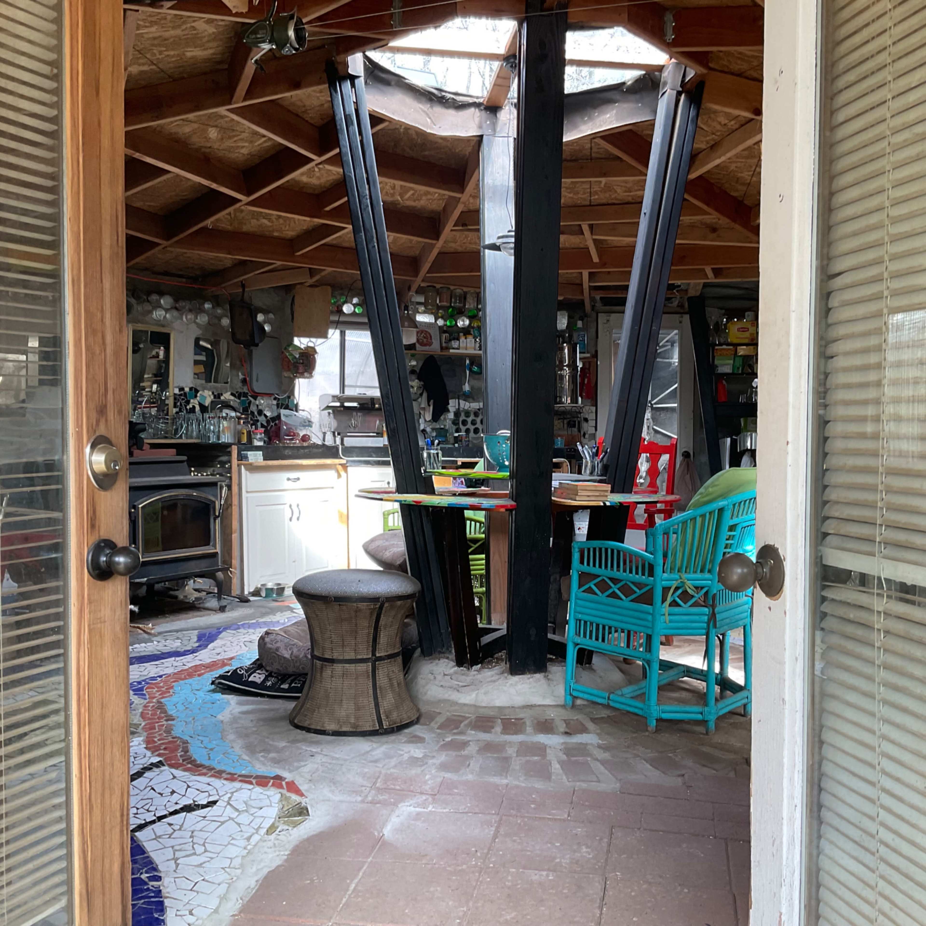 The interior of a rustic kitchen and dining area with a circular wooden table, colorful chairs, and a central black support beam.