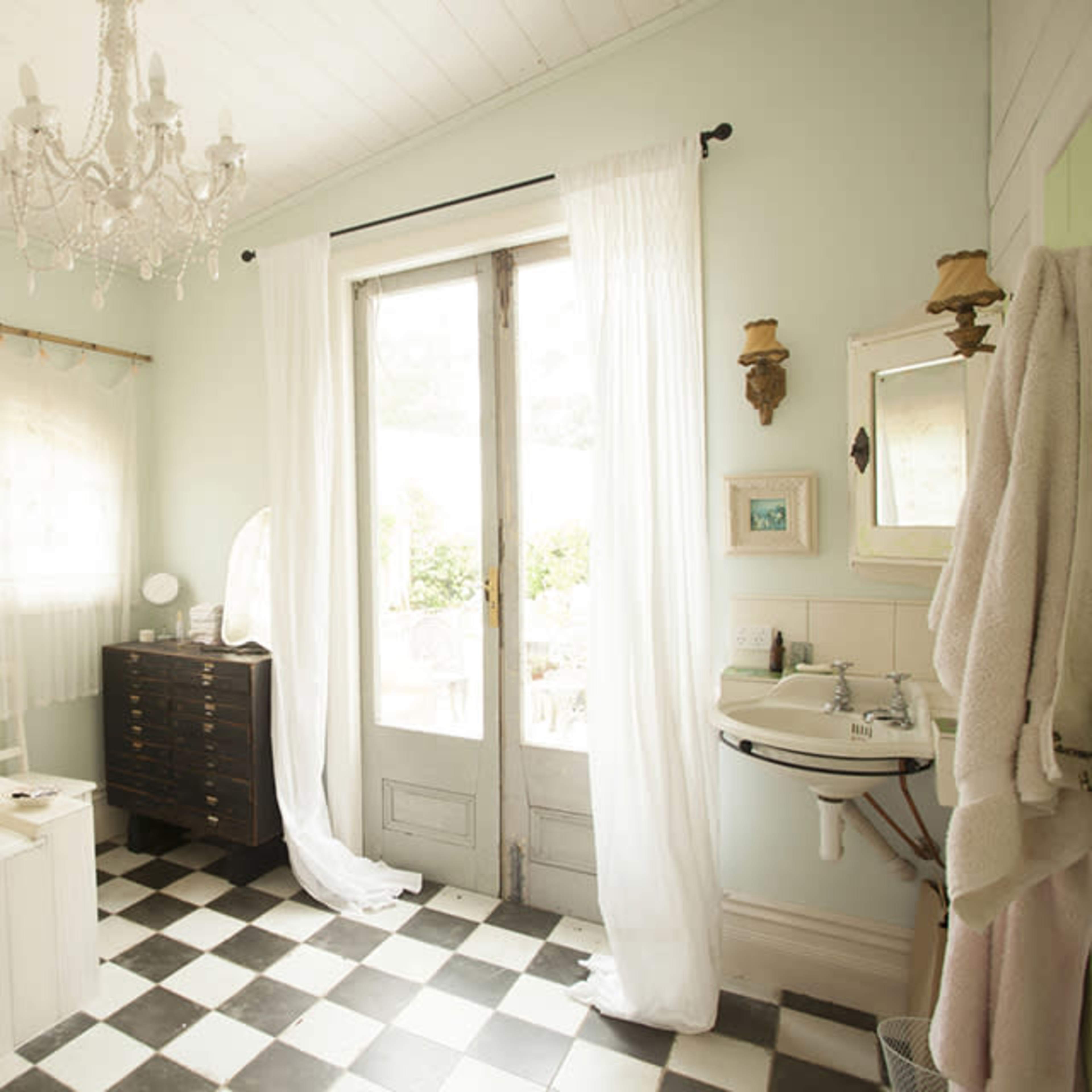 The bathroom features a white bathtub, a checkered black-and-white floor, and large windows draped with sheer curtains.