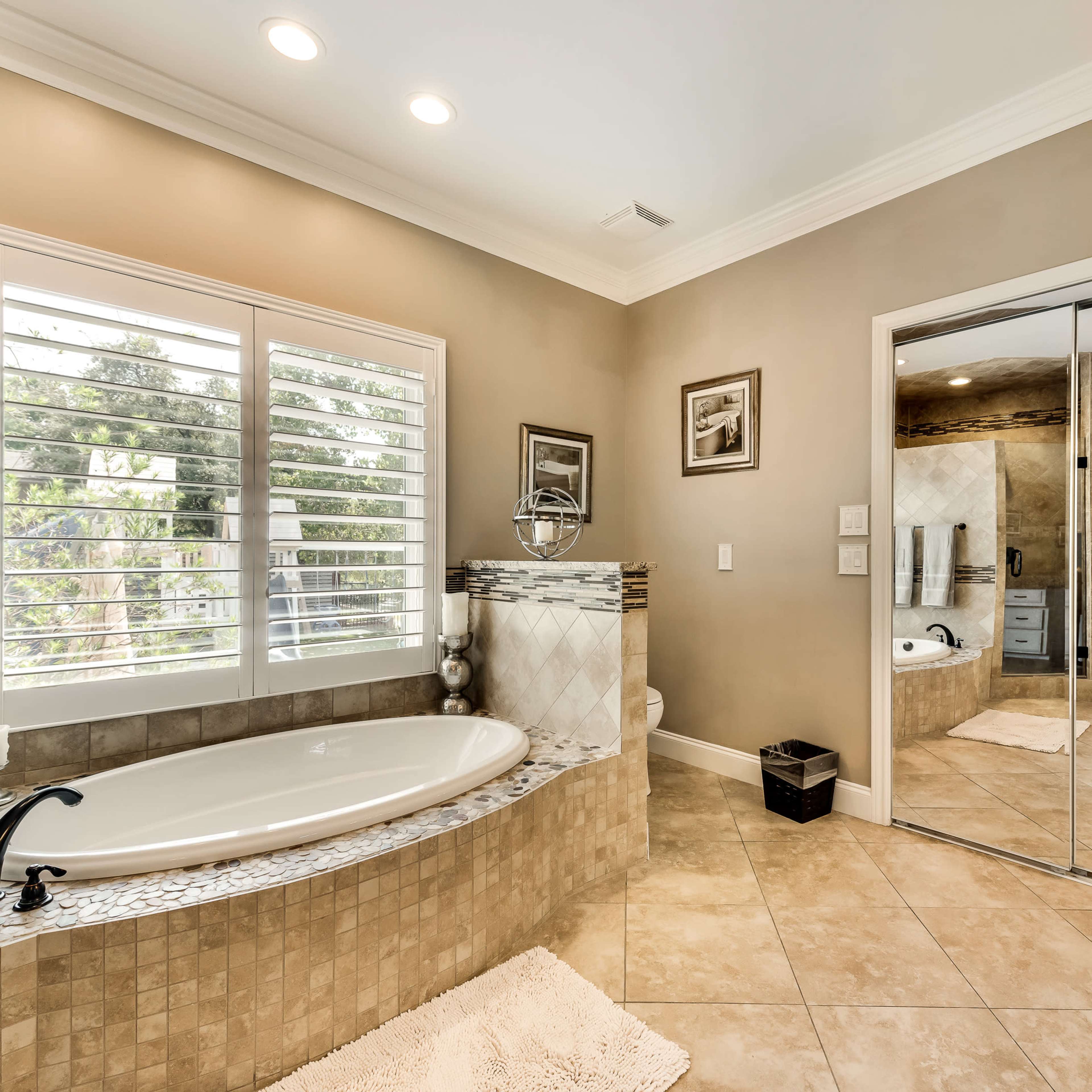 A spacious bathroom with a large bathtub, dual sinks, and a mirrored closet reflecting the room's features.
