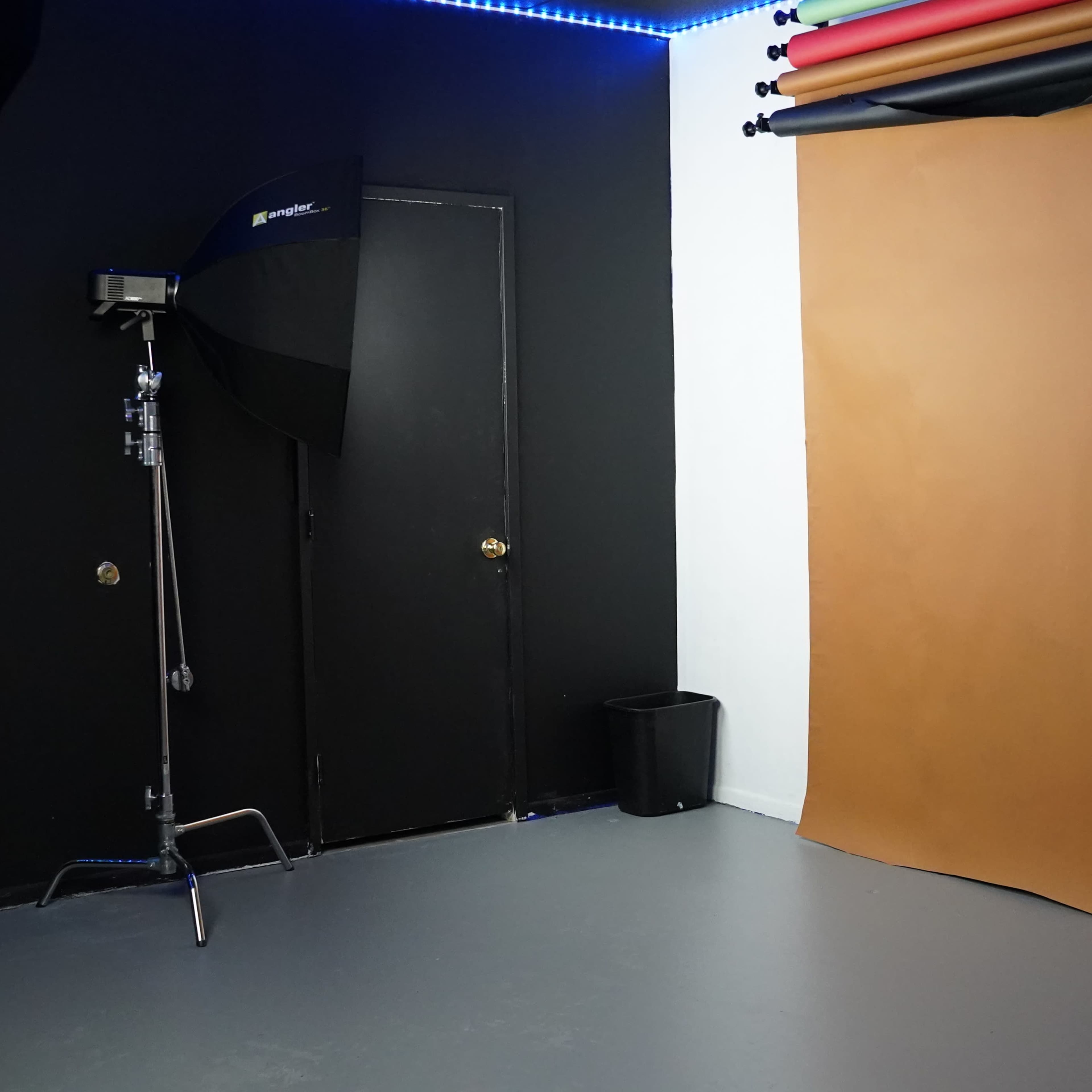 A photography studio setup with a brown backdrop, a black door, and a light stand in the corner.