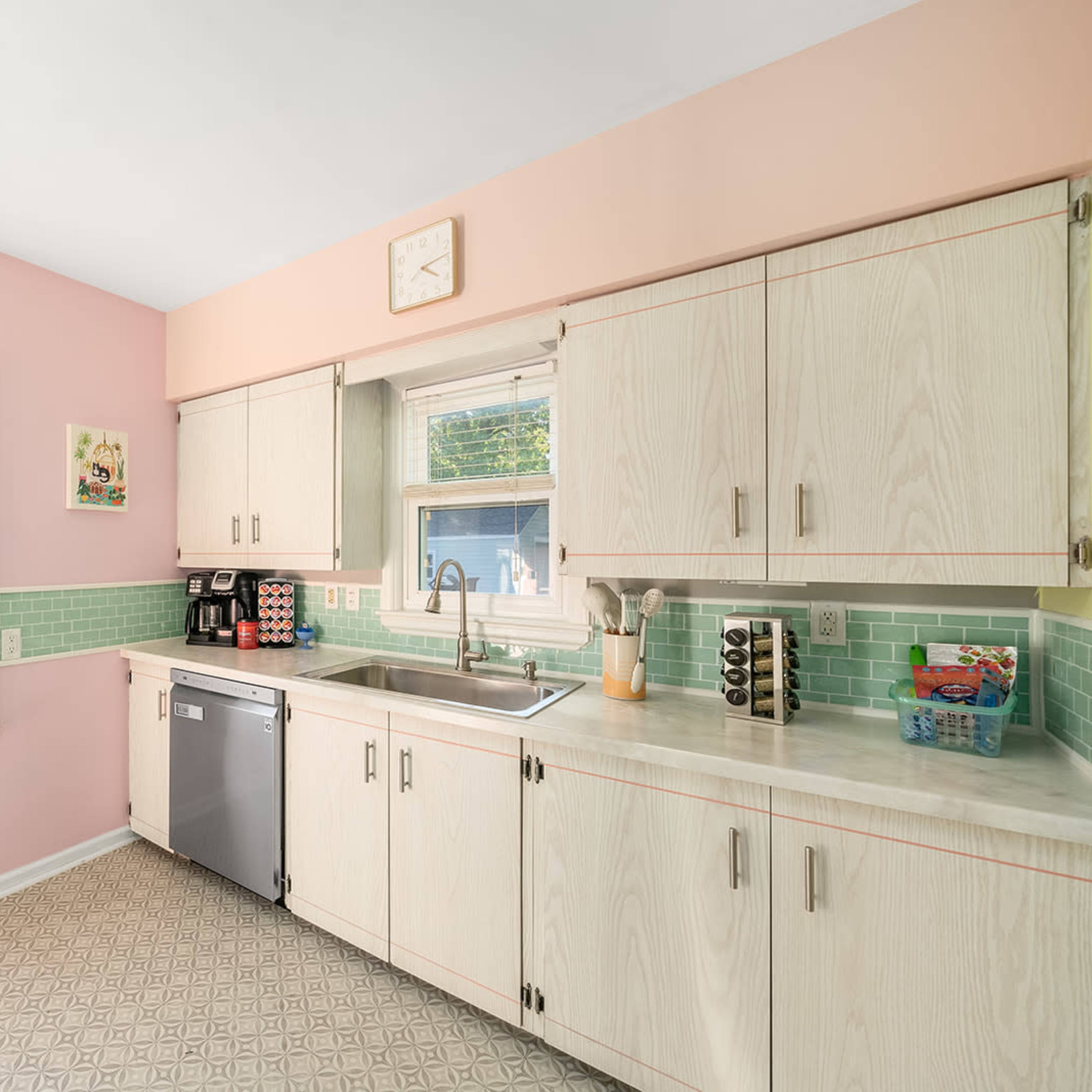 The kitchen features light pink walls, beige cabinetry, a stainless steel dishwasher, and a window above the sink.
