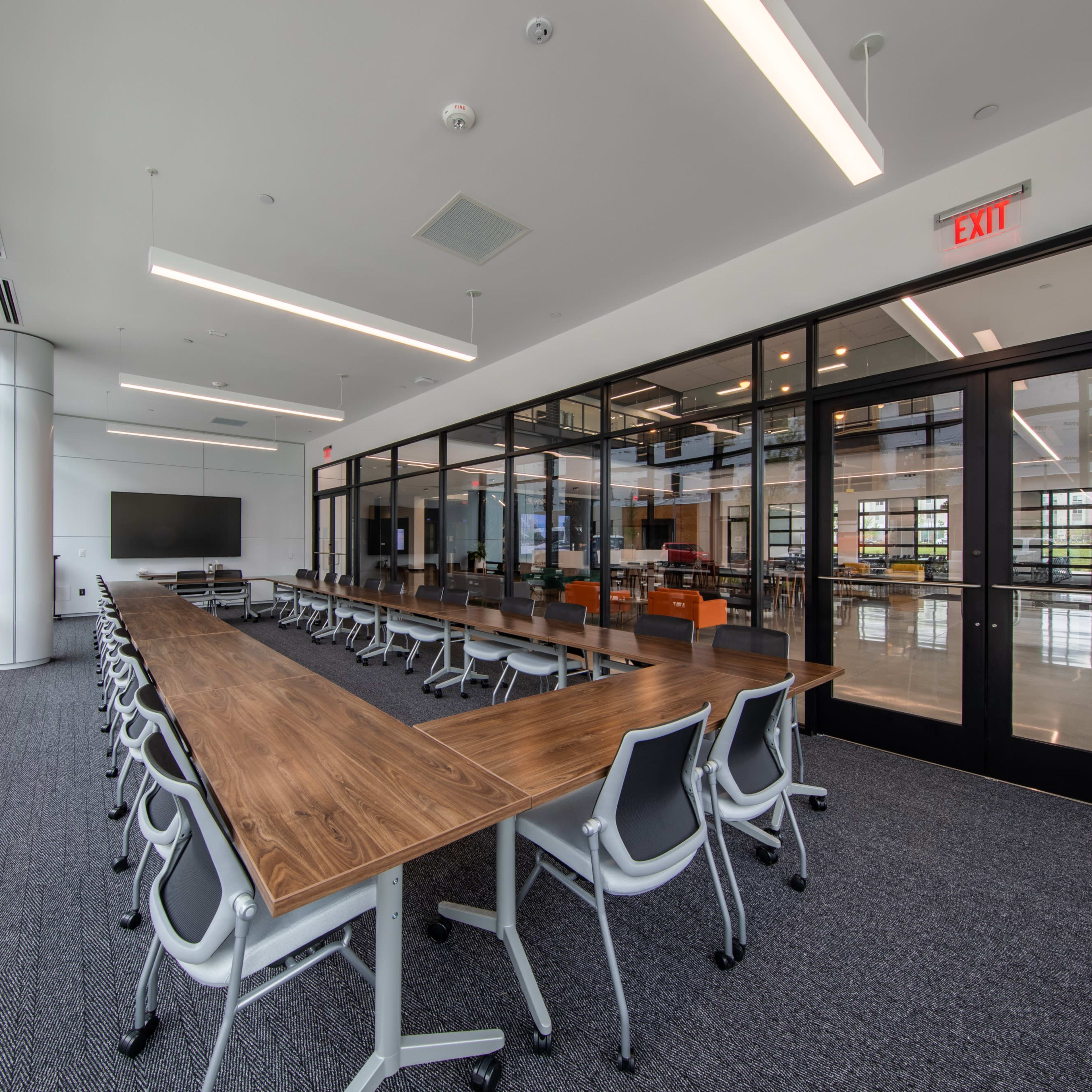 A modern conference room features a long wooden table surrounded by ergonomic chairs, with large windows allowing natural light to fill the space.