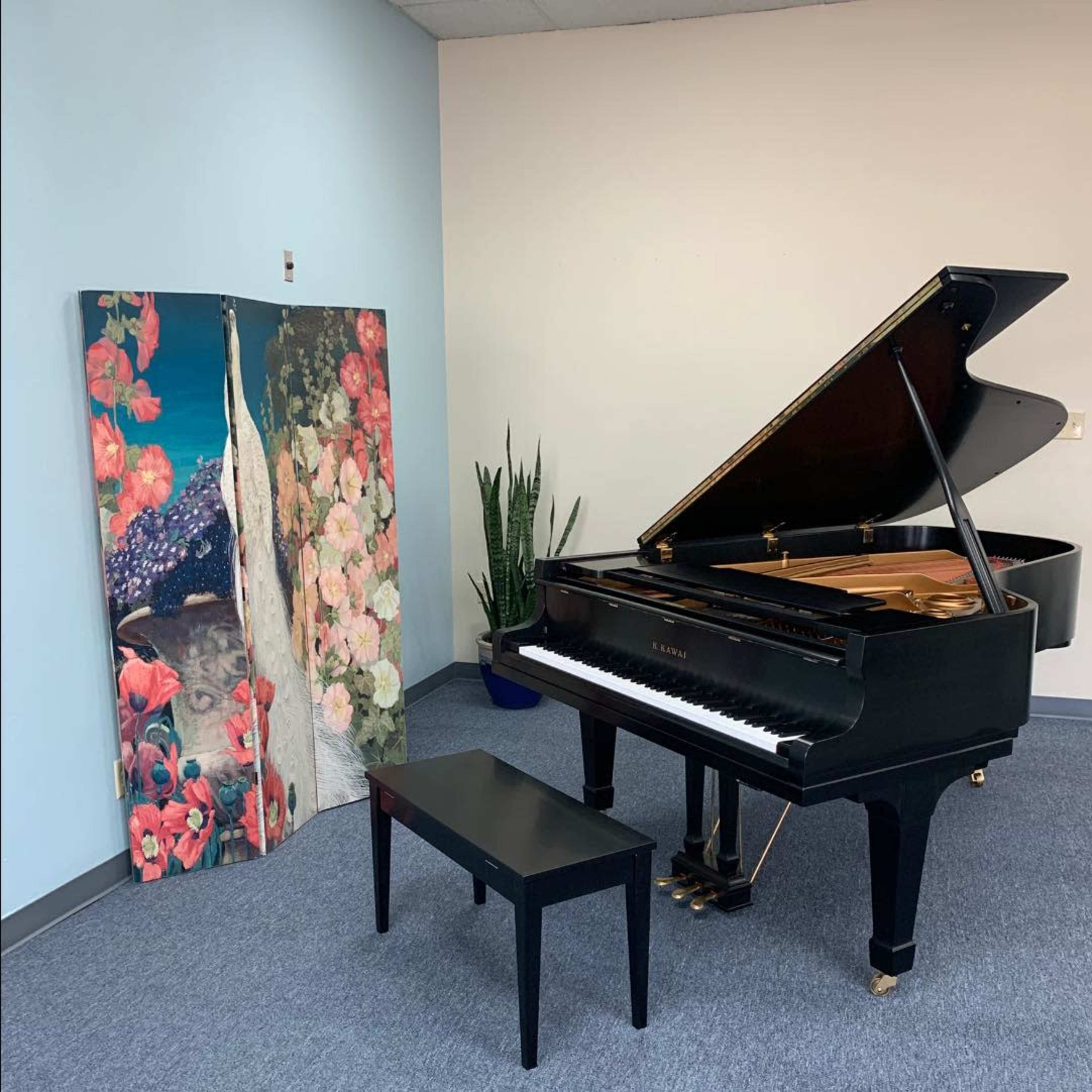 A black grand piano is positioned next to a large, vibrant artwork featuring a peacock and flowers in a room with light blue walls.