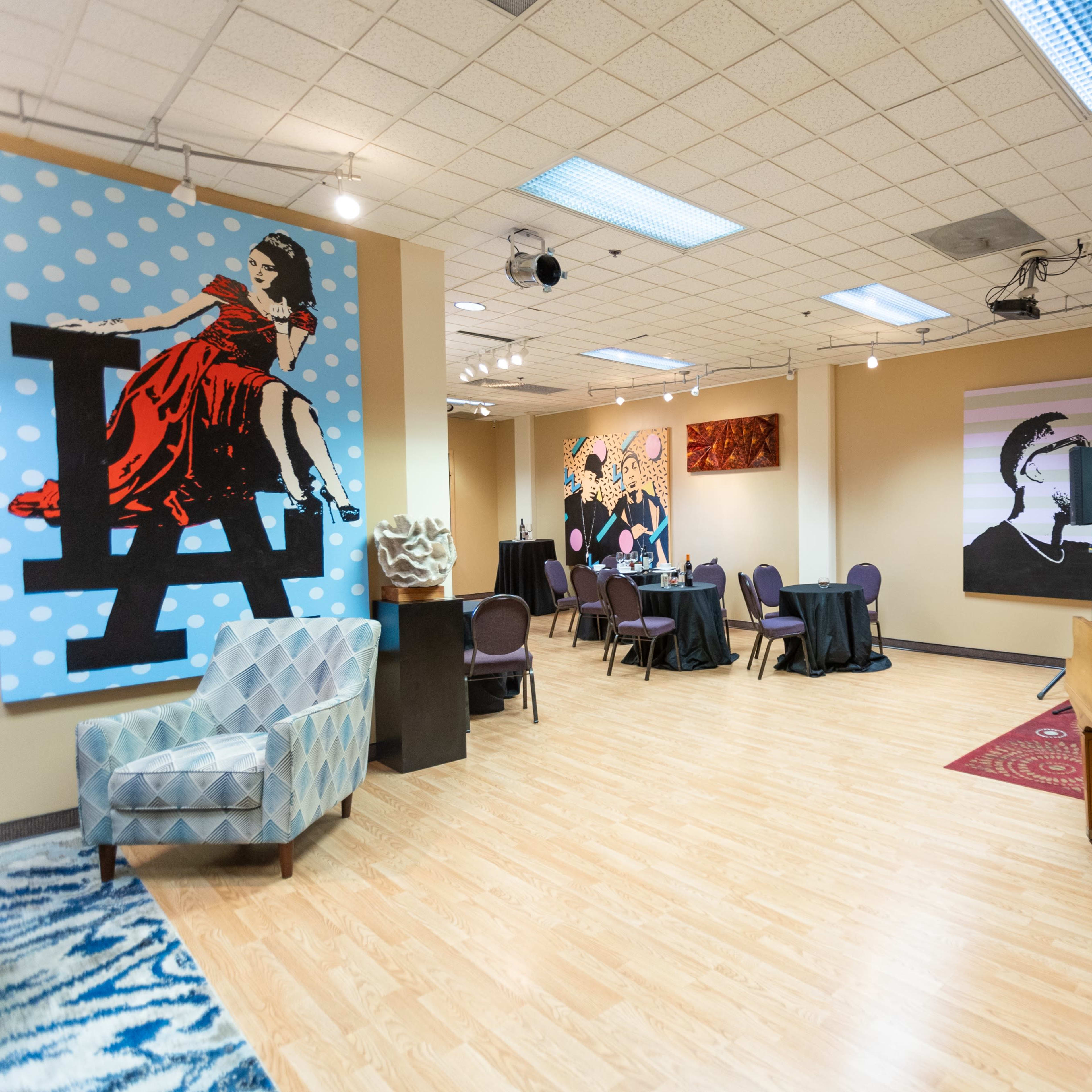 A spacious art-filled lounge with a piano, tables set for dining, and colorful murals on the walls.
