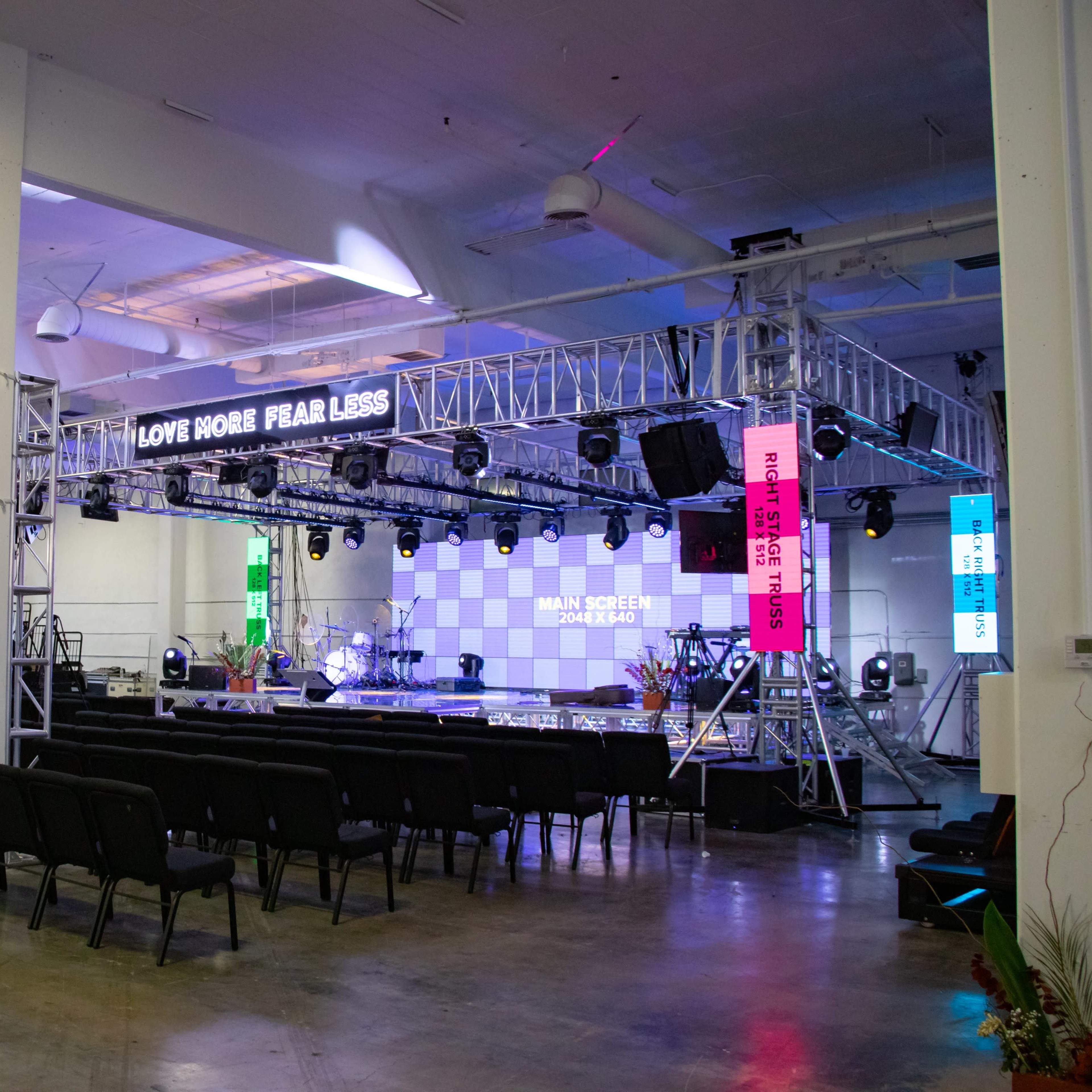 A spacious event venue set up with a stage, seating arrangements, and colorful lighting fixtures.
