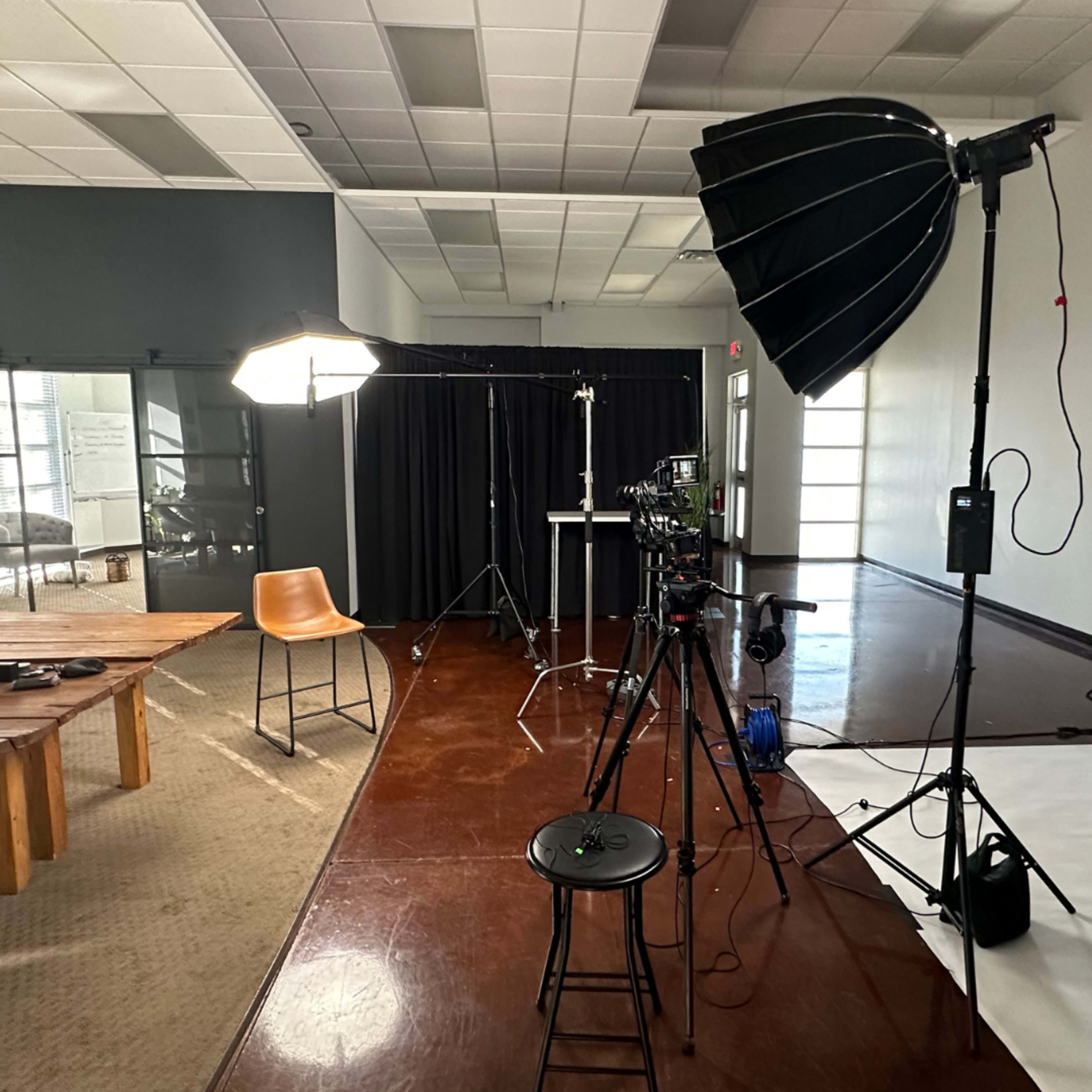A photography studio setup with various lighting equipment, a backdrop, and chairs arranged around a wooden table.