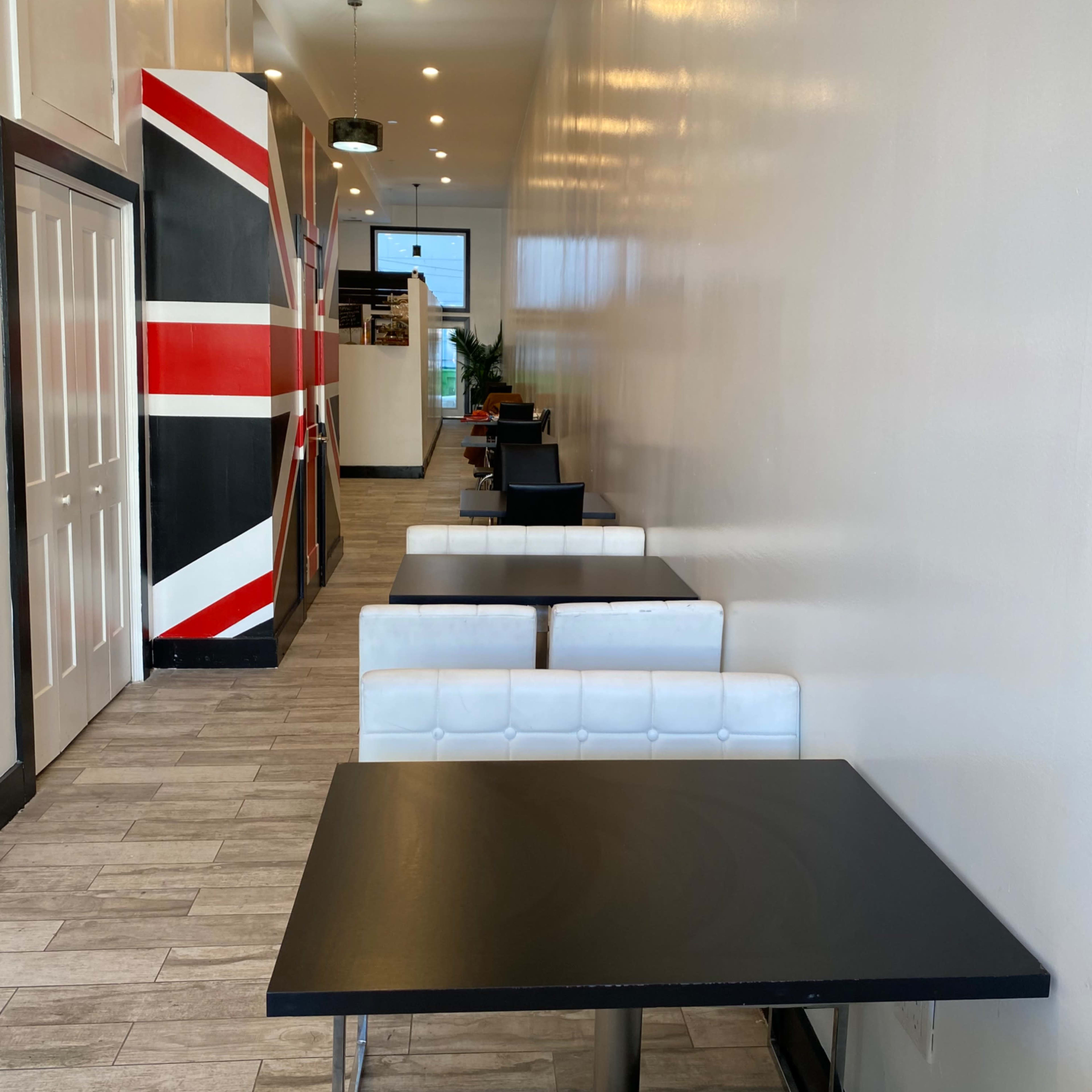A long, narrow cafe interior with white walls, black tables, and a prominent red and white geometric design on one side.