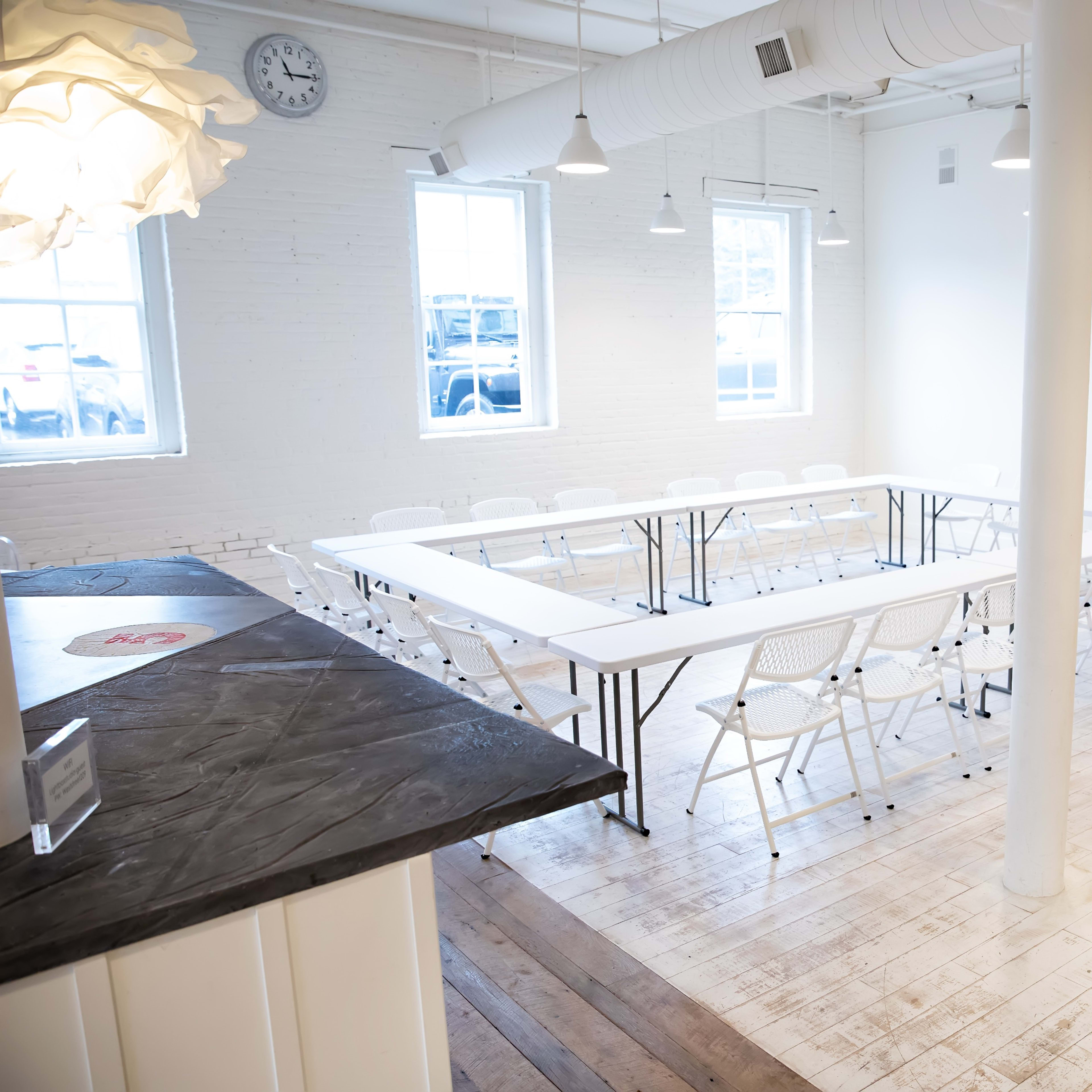 A bright, minimalist meeting room arranged with a rectangular table made of folding chairs.