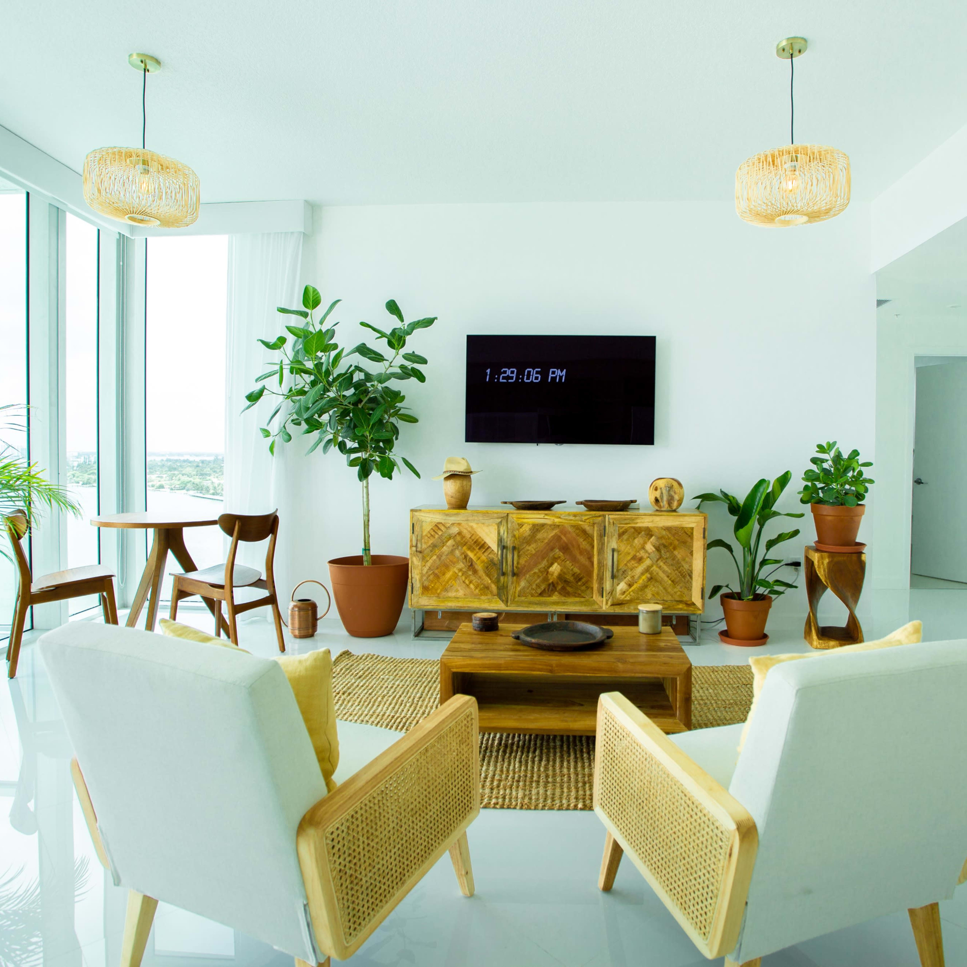 A modern living space features two armchairs facing a wooden coffee table, flanked by potted plants and a wall-mounted television.