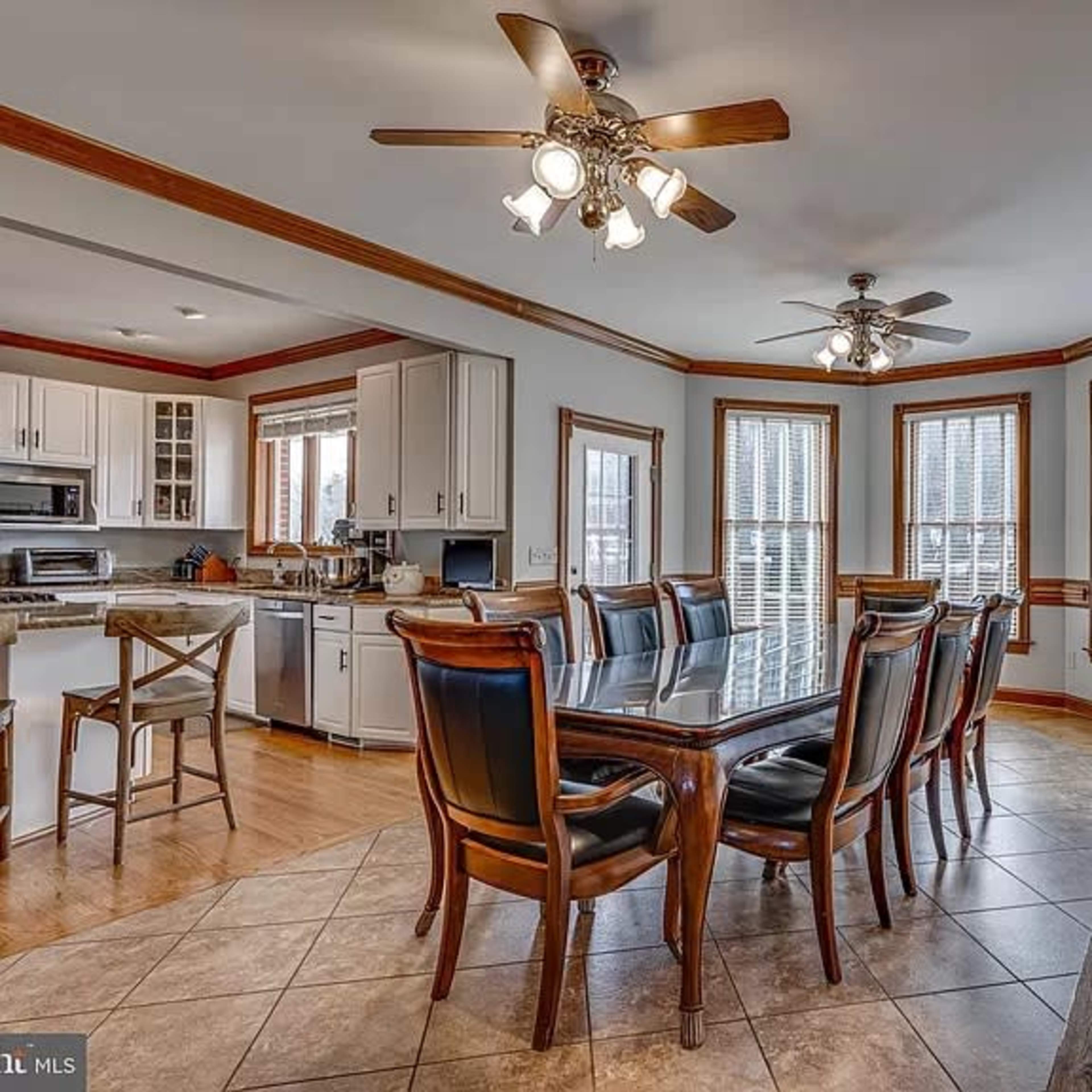 A spacious dining area features a large table surrounded by wooden chairs, with multiple windows allowing natural light to enter.