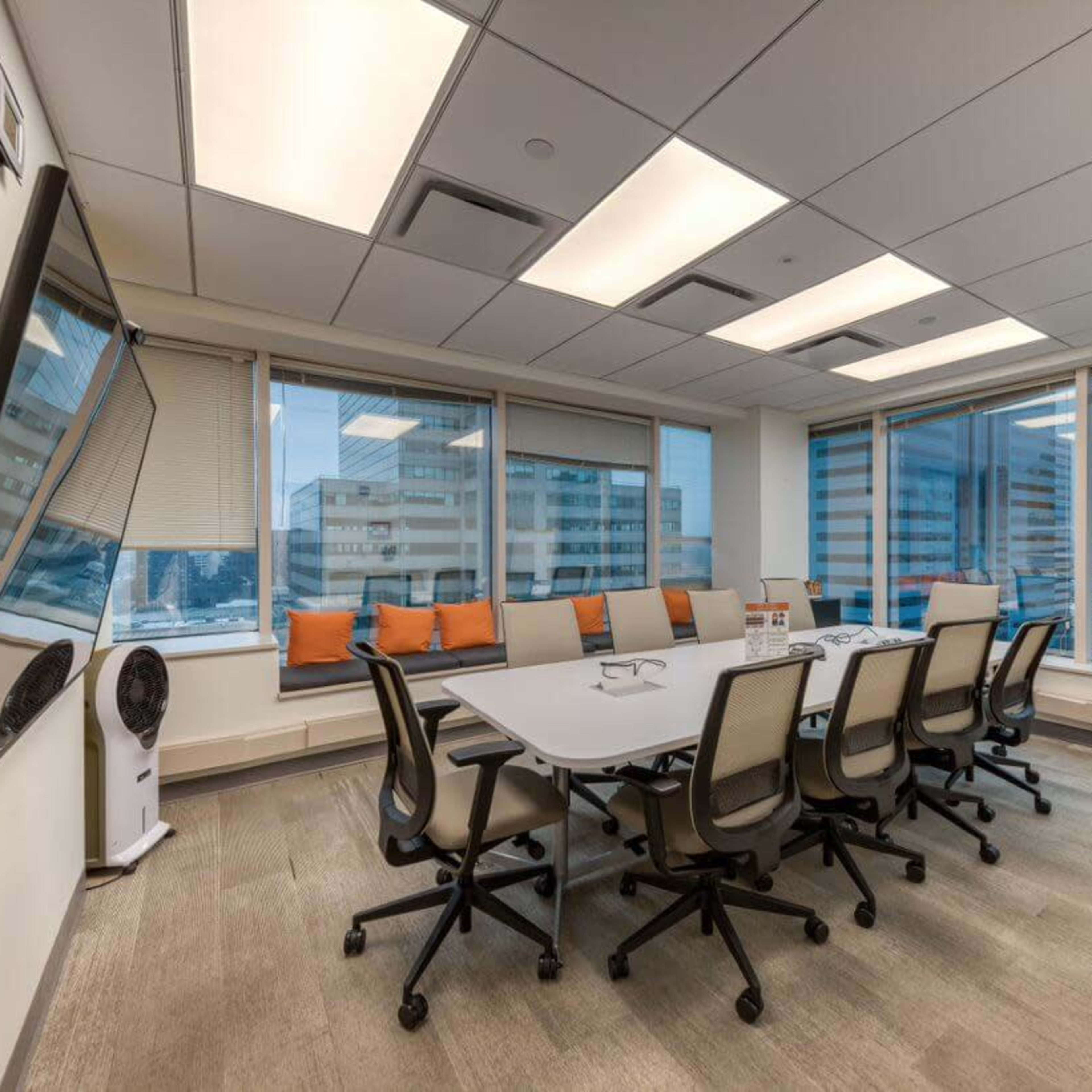 A conference room with a large table, multiple chairs, a flip chart, and large windows showcasing a city view.