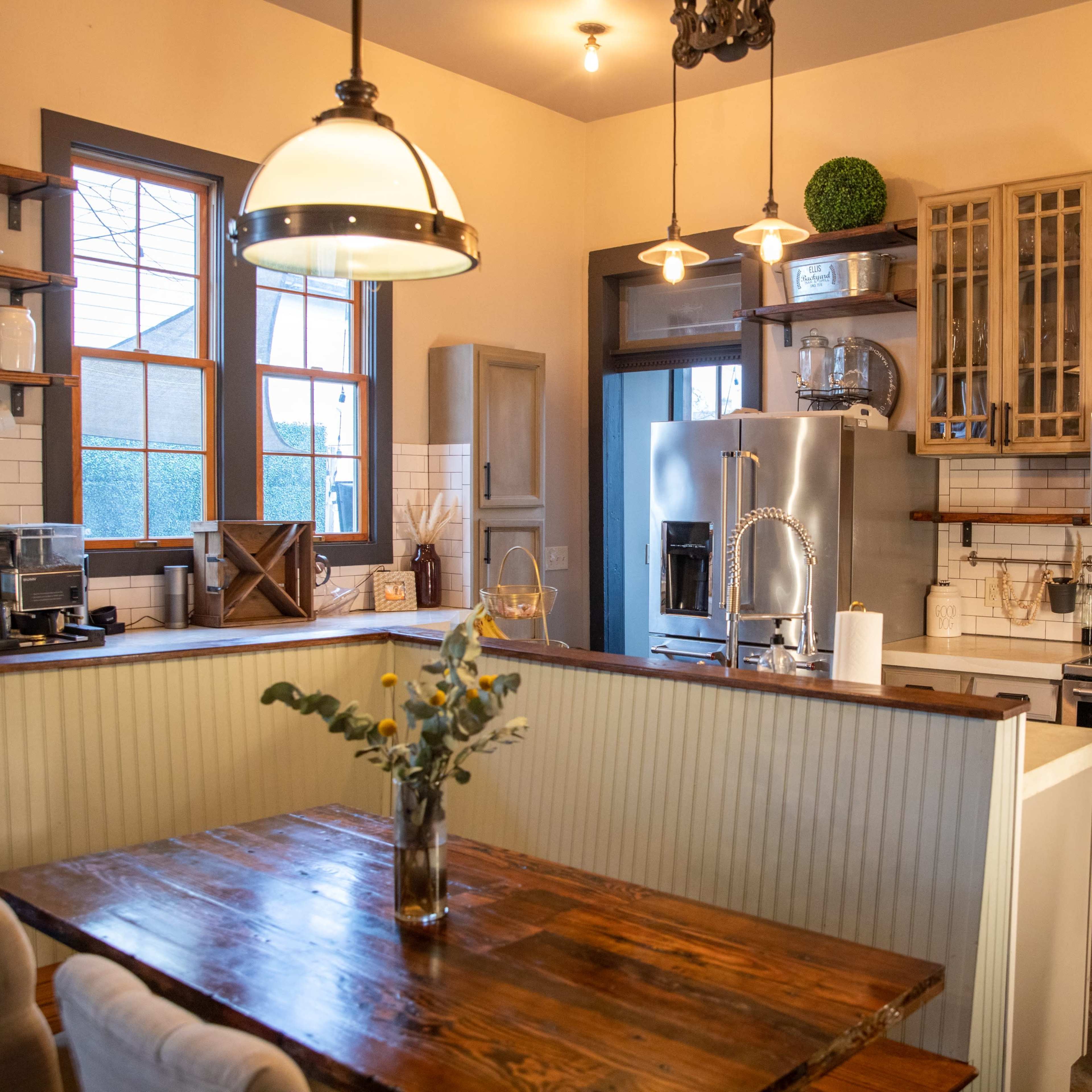 A kitchen featuring wooden shelves, a stainless steel refrigerator, an oven, and a dining table with flowers in a vase.
