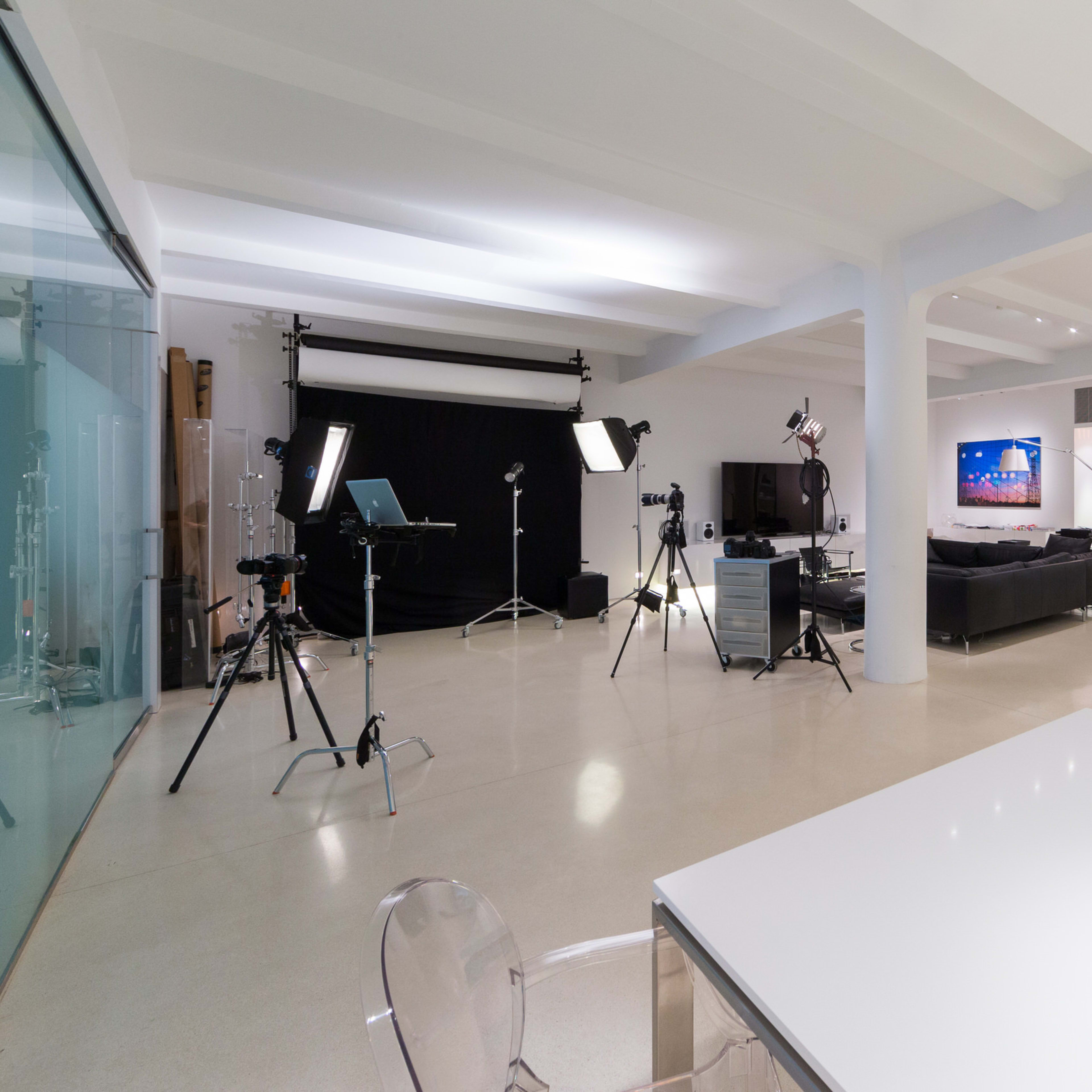 A modern studio space equipped with filming equipment, a seating area, and a kitchen counter.