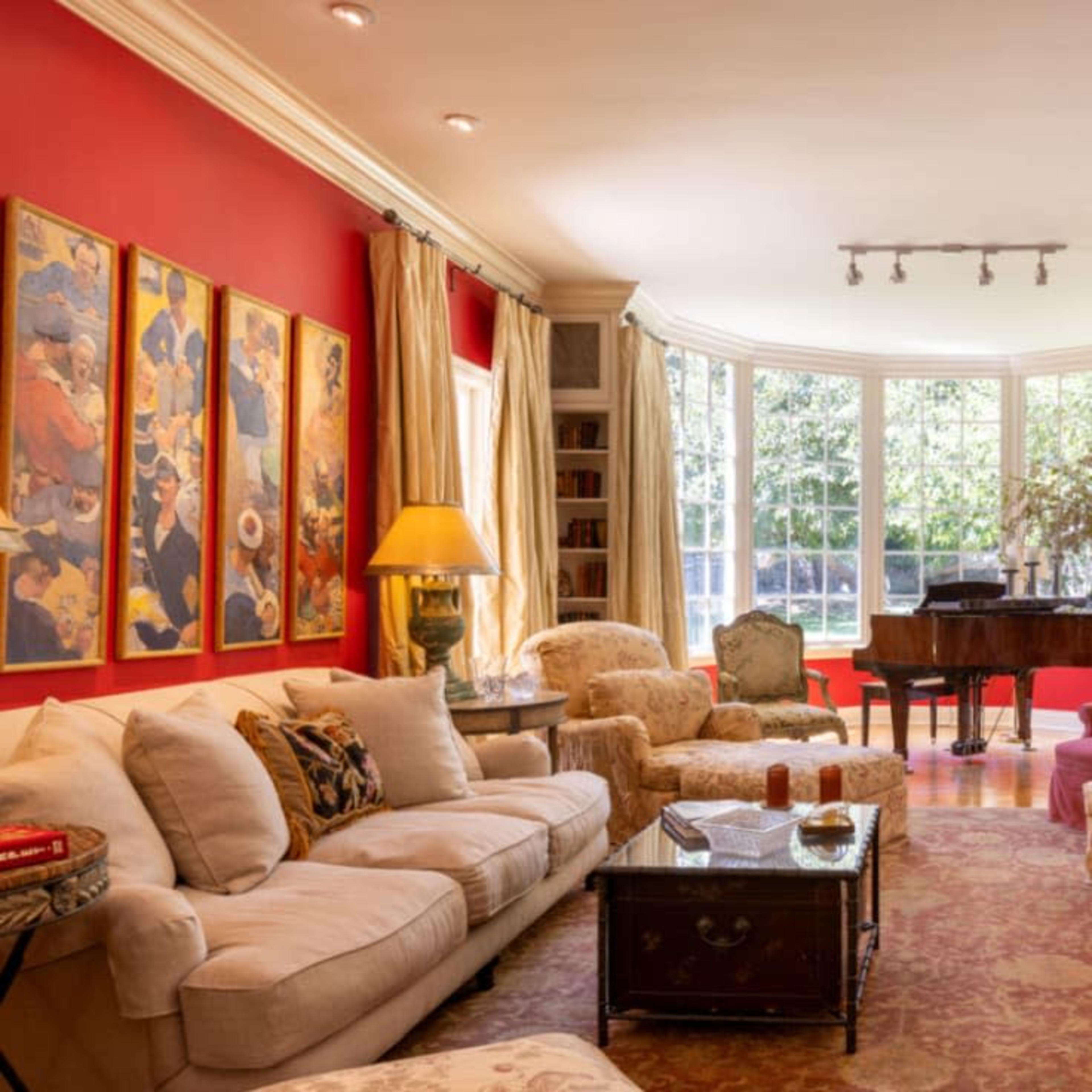 A cozy living room with red walls, a grand piano, and several comfortable seating arrangements around a coffee table.