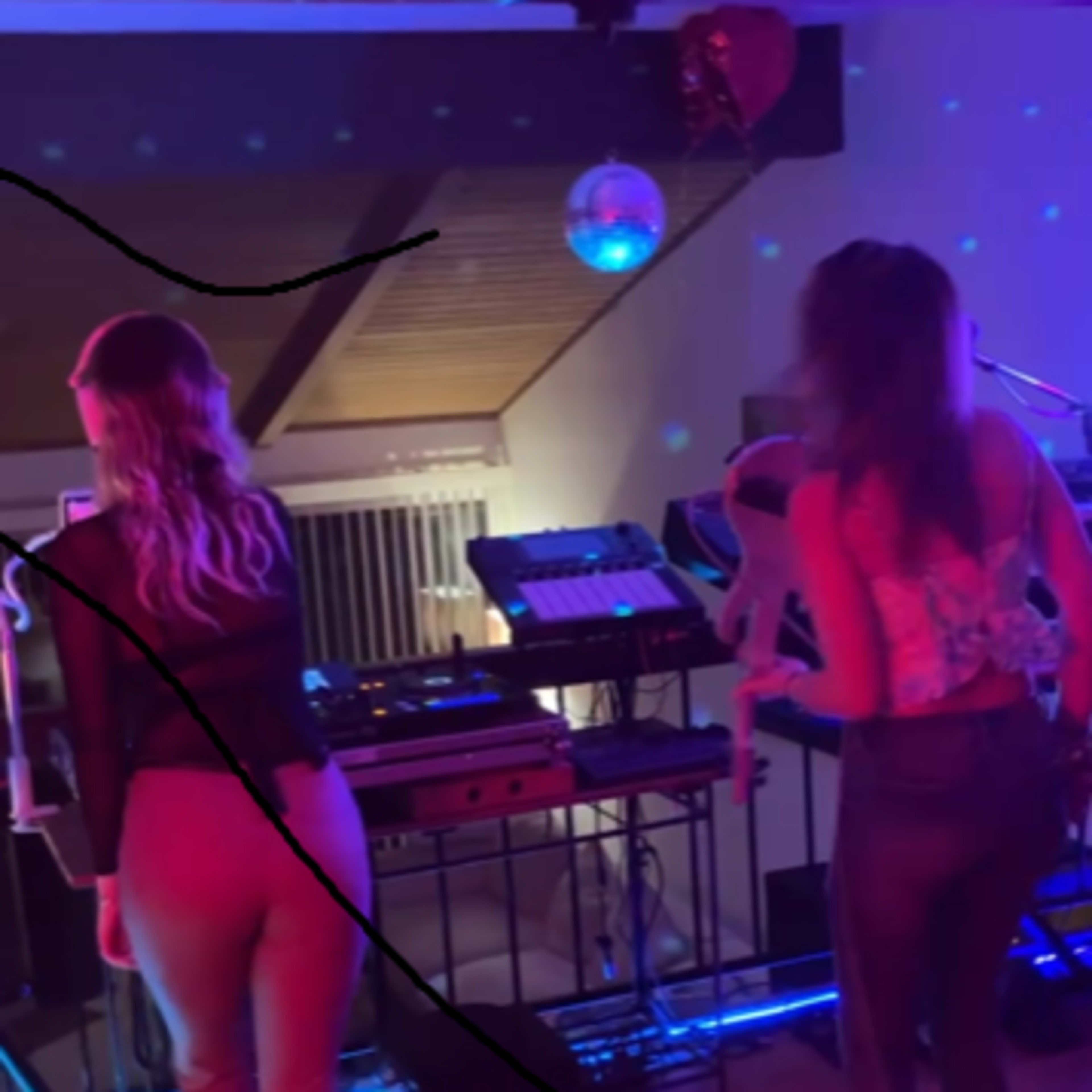 Two women perform on stage with musical equipment and colorful lights in the background.